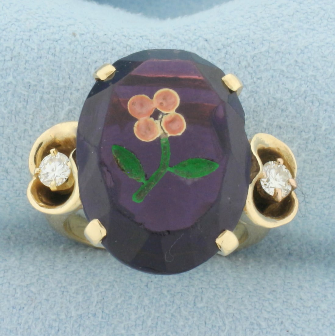 Hand Painted Amethyst and Diamond Flower Ring in 14k Yellow Gold: In 14k yellow gold. Contains on 20mm by 14.5mm high quality natural oval cut amethyst gemstone with a hand carved and painted flower design. Small chip on amethyst. Also contains two 1/8ct high qualit