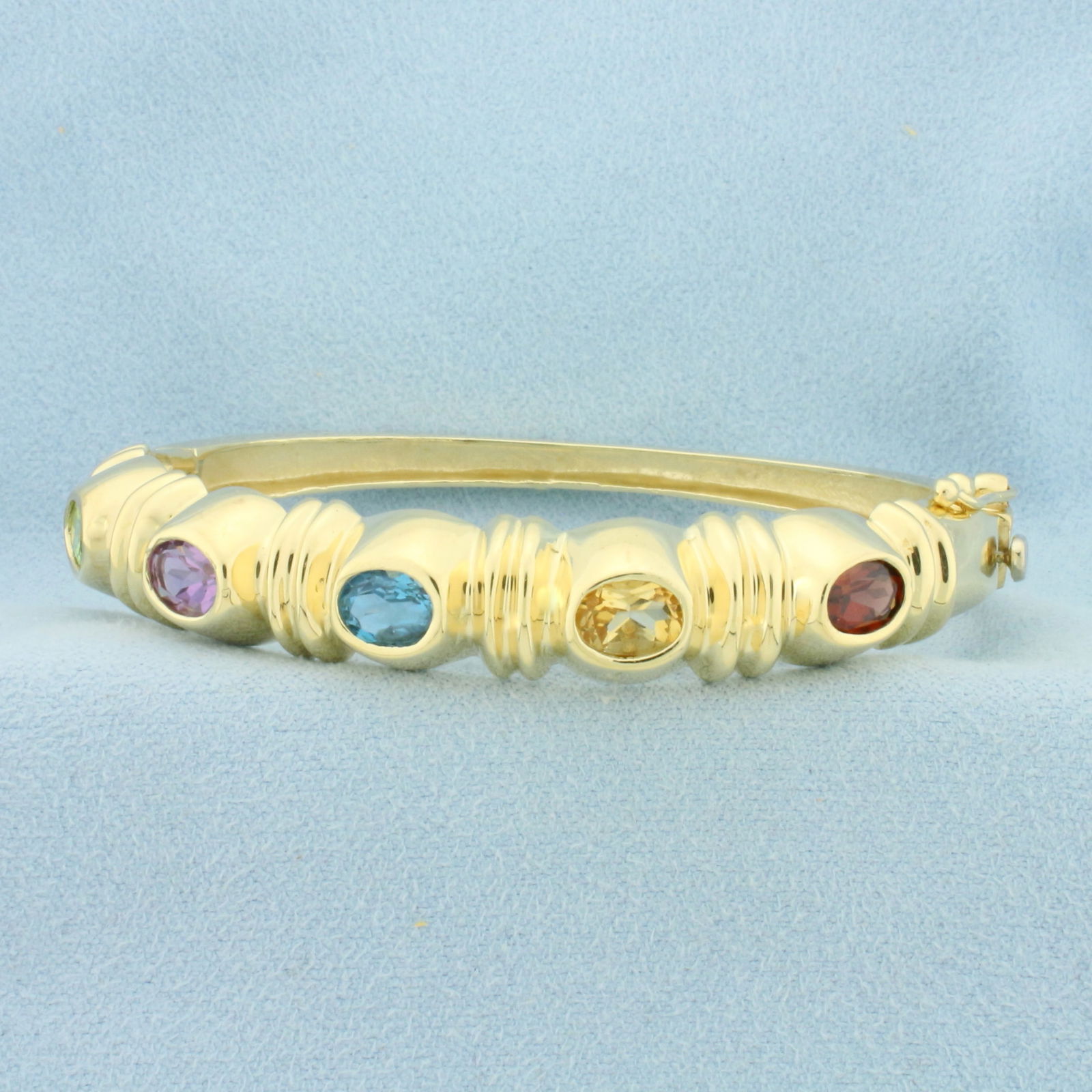 Rainbow Gemstone Bangle Bracelet in 14k Yellow Gold: In 14k Yellow Gold. Contains five 5x7mm high quality natural gemstones including: Peridot, Amethyst, Blue Topaz, Citrine, and Garnet. Interior dimensions: 2 1/4 inch by 2 inch. 10mm wide. Hinged openi