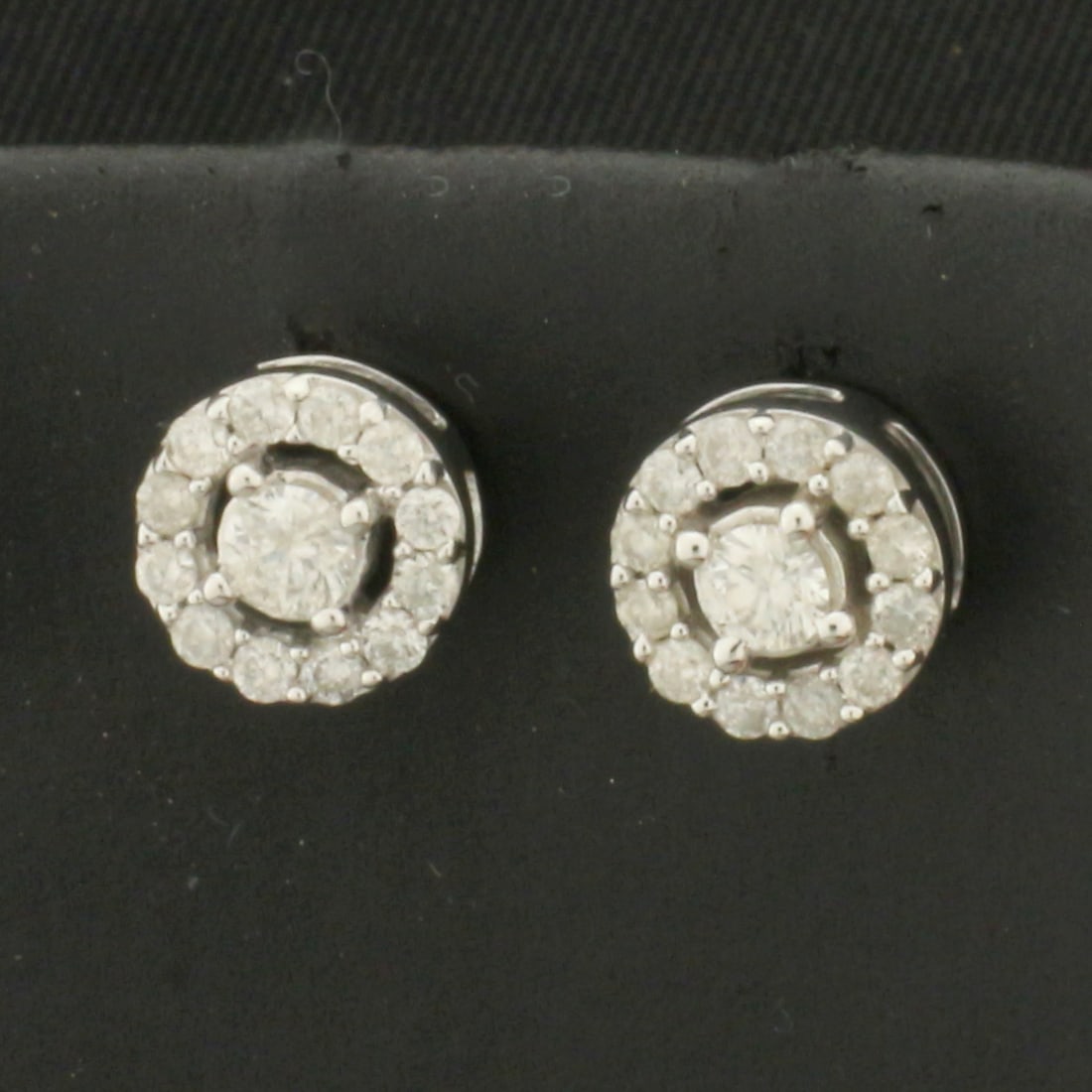 Diamond Halo Stud Earrings in 10k White Gold: In 10k White Gold. Contains two .10ct and twenty-four .01ct high quality diamonds, SI clarity/H color. 7.5mm diameter. Friction backs. 1.9g.