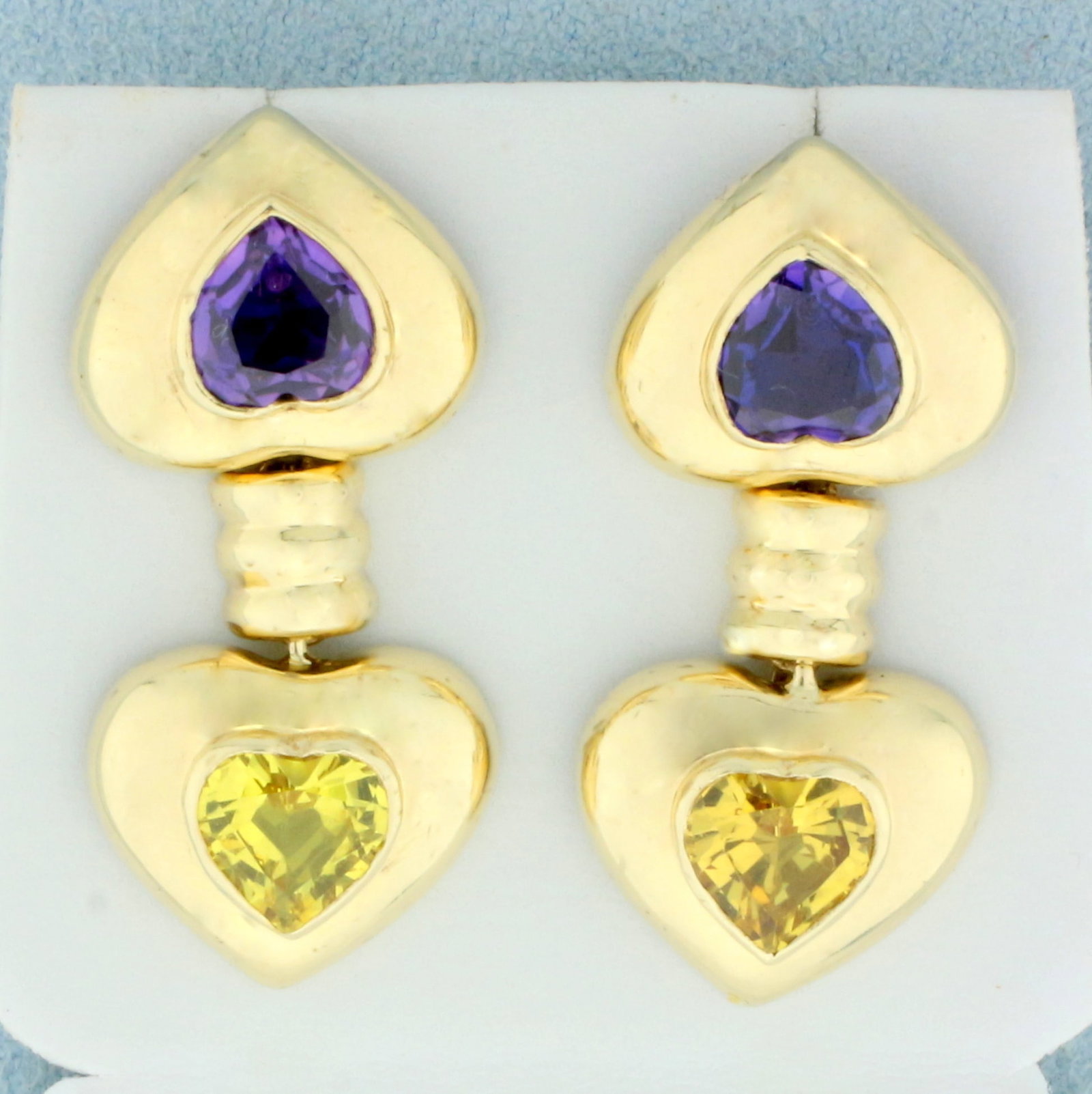 Designer Purple and Yellow Sapphire Dangle Heart Earrings in 14K Yellow Gold: In 14K Yellow Gold. Each earring contains one high quality natural 7mm heart cut Purple and one Yellow Sapphire gemstone, with intense color and excellent clarity. 1 1/4 inches long. 3/4 inch wide. 7.