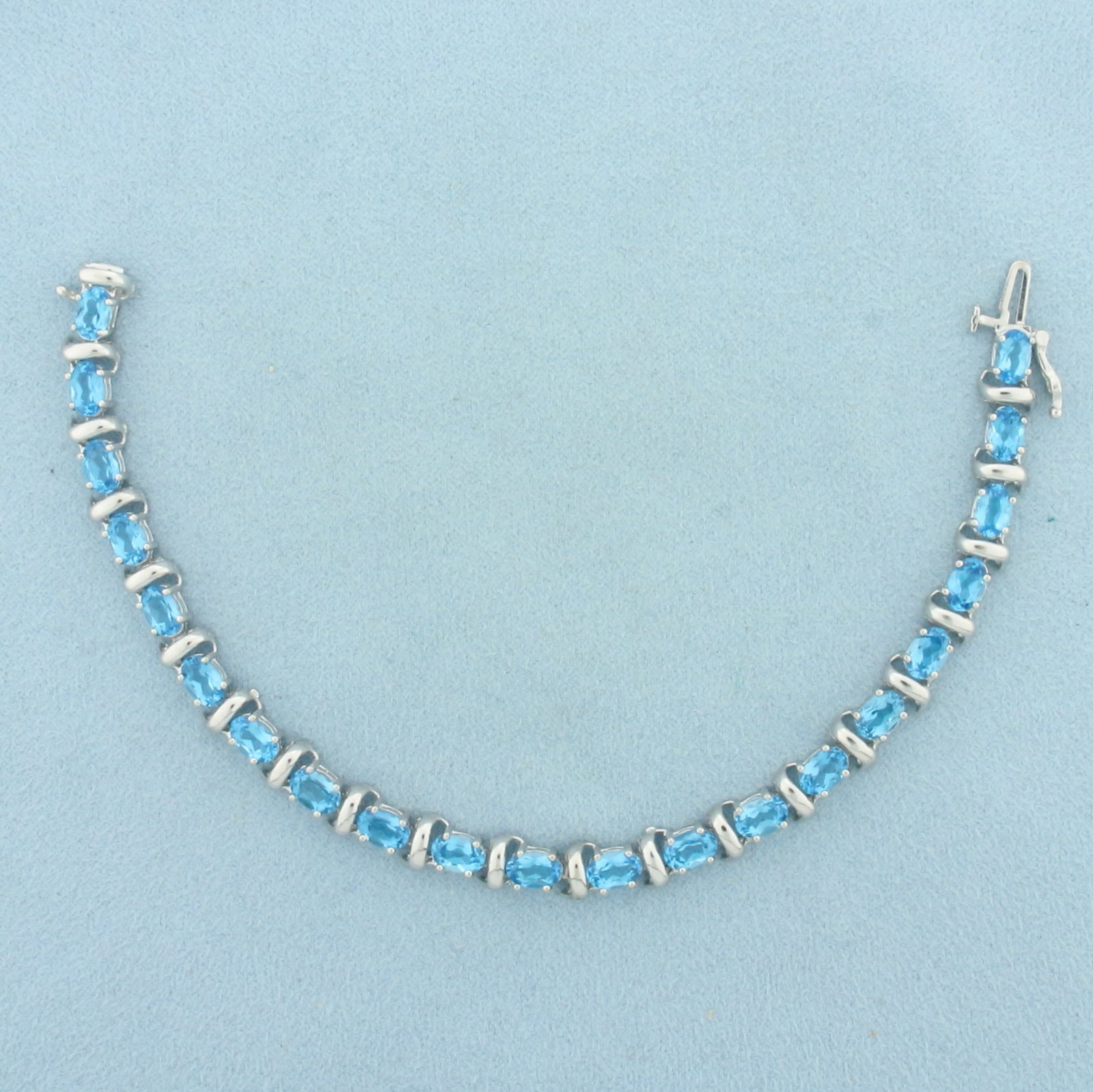 Swiss Blue Topaz Tennis Bracelet in 14k White Gold: In 14k White Gold. Contains twenty-one 4x6mm high quality oval cut natural Blue Topaz gemstones, approximately 10ct TW, with electric blue color and excellent clarity. 7 inches long. 6mm wide. Slide c