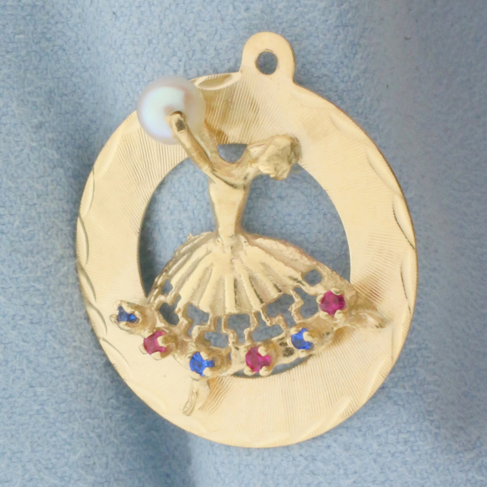 Pearl, Ruby, and Sapphire Dancer Charm or Pendant in 14k Yellow Gold: In 14k Yellow Gold. Contains one high quality 4.5mm cultured pearl with high luster. Pearl spins within dancer's outstretched arms. Also contains three high quality 1.5mm sapphire and ruby gemstones w