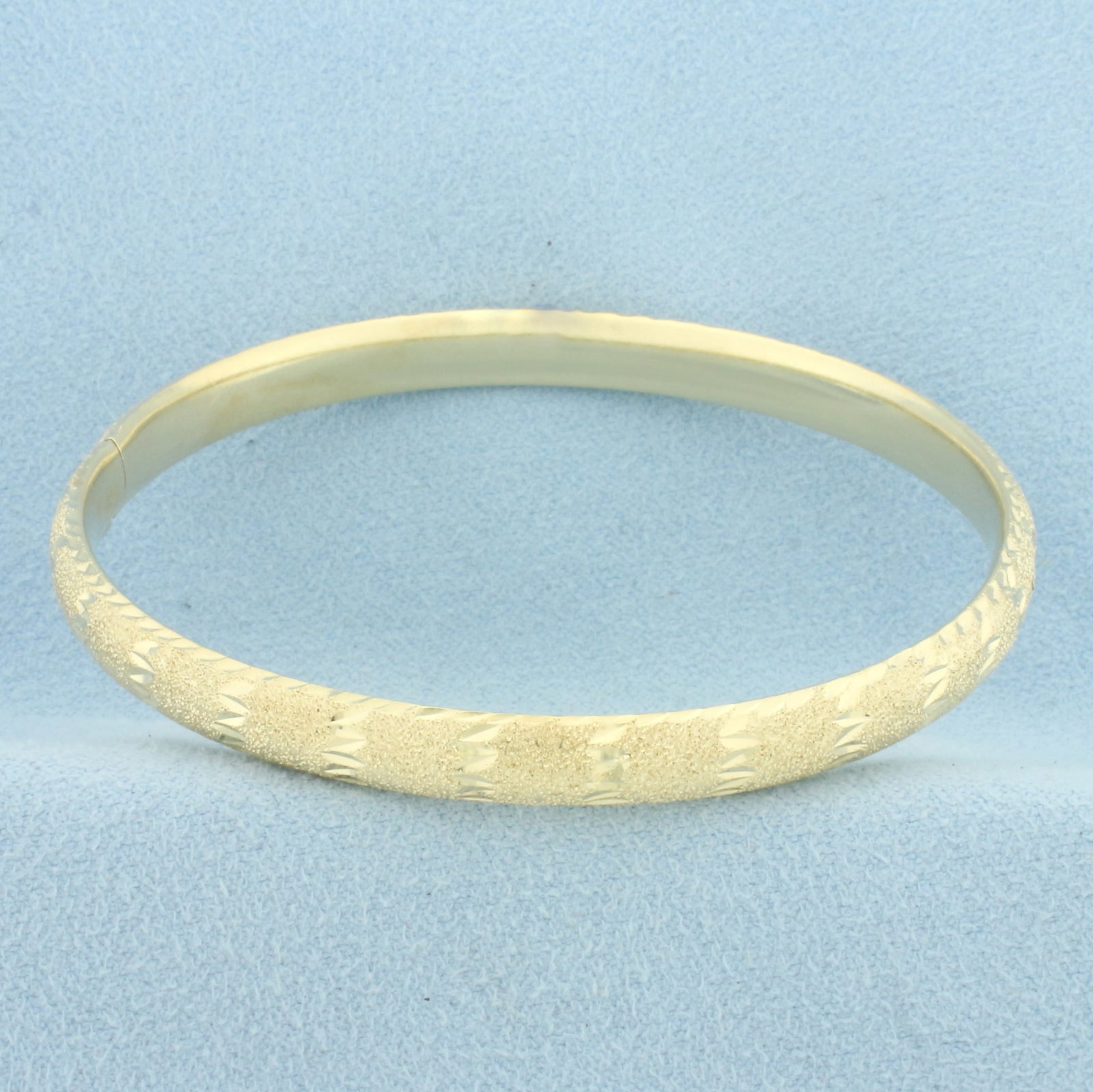 Sandblast and Diamond Cut Finish Hinged Bangle Bracelet in 14k Yellow Gold: In 14k Yellow Gold. Interior dimensions: 2 3/8 inch x 2 1/4 inch. 6.2mm wide. Hinged design with locking slide clasp. 8.1g.