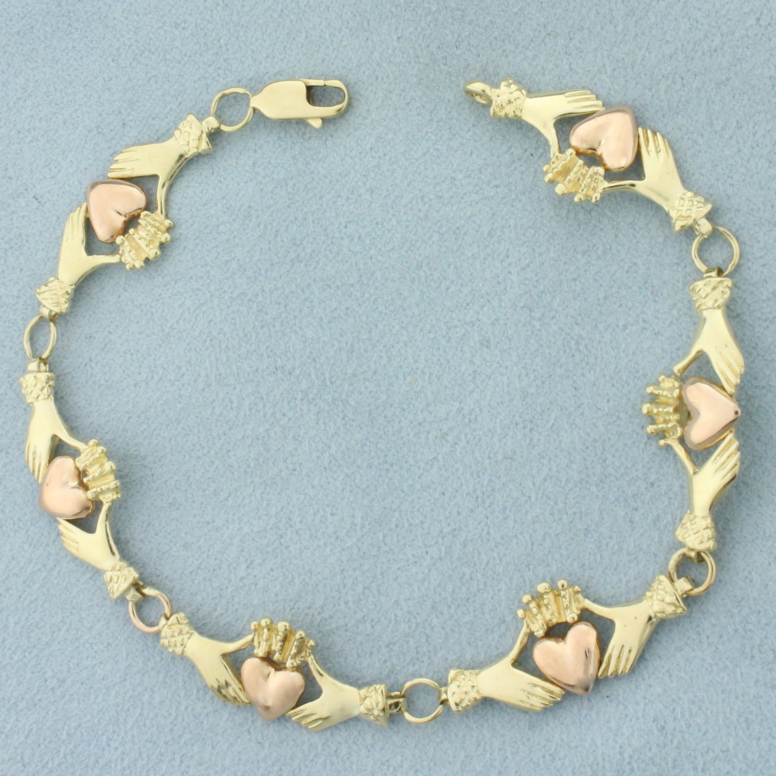 Claddagh Bracelet in 14k Yellow and Rose Gold: In 14k Yellow and Rose Gold. 7 1/4 inches long. 3/8 inch wide. Lobster clasp. 8.6g