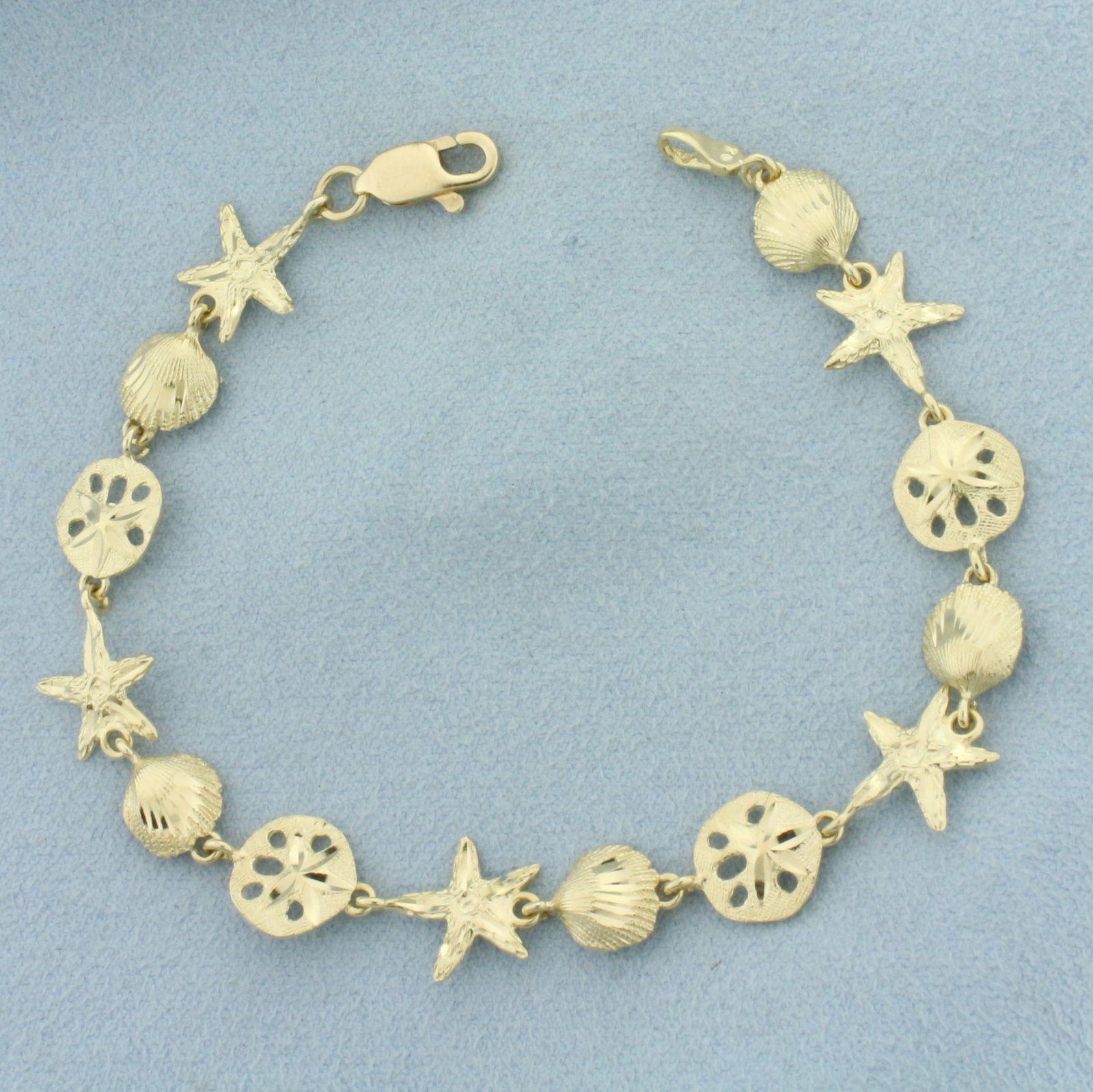 Sea Life Starfish Seashell Sand Dollar Bracelet in 14k Yellow Gold: In 14k Yellow Gold. 7 3/8 inches long. 3/8 inch wide. Starfish, seashells, and sand dollar design. Lobster clasp. 5.8g.