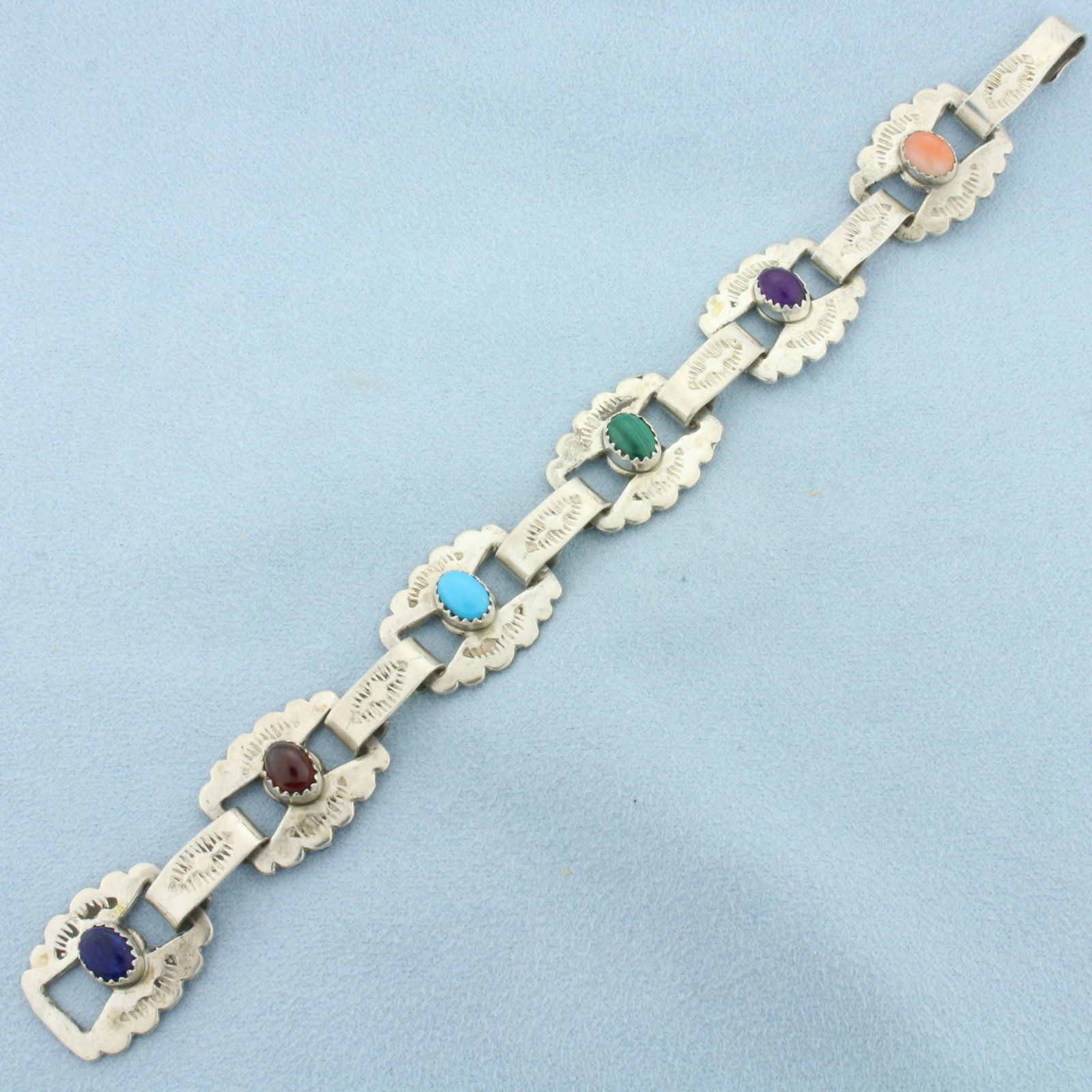 Multi-Gemstone Bracelet in Sterling Silver: In .925 Sterling Silver. Contains six 8x6mm high quality cabochon gemstones including: Coral, Amethyst, Malachite, Turquoise, Garnet, and Lapis Lazuli. 7 1/8 inch long. 5/8 inch wide. 25.1g.