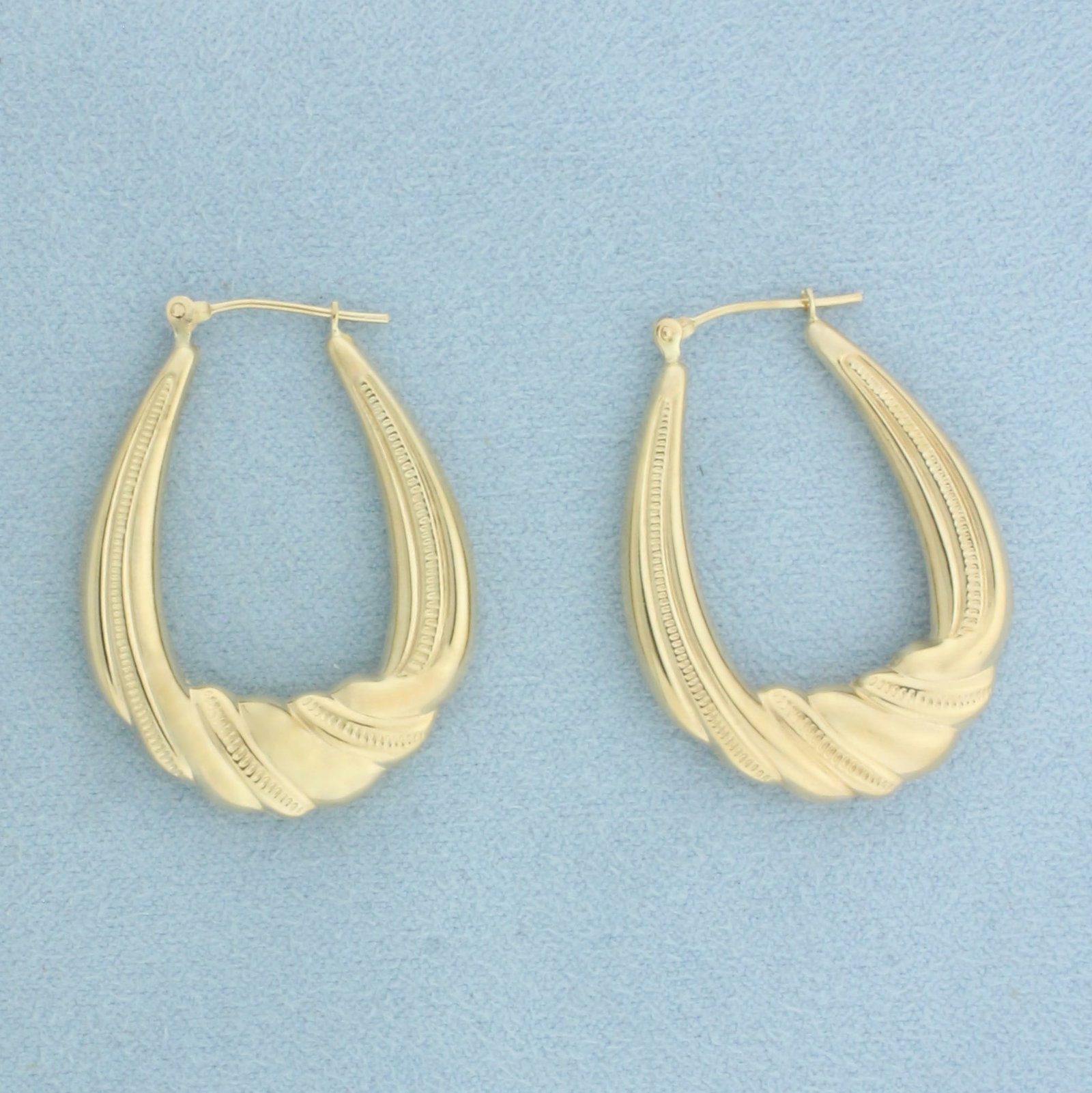 Twisting Hoop Earrings in 10k Yellow Gold: In 10k Yellow Gold. 1 1/4 inch long. 1 inch diameter. 8.2mm wide at widest point. Hinged closure. 2.6g.