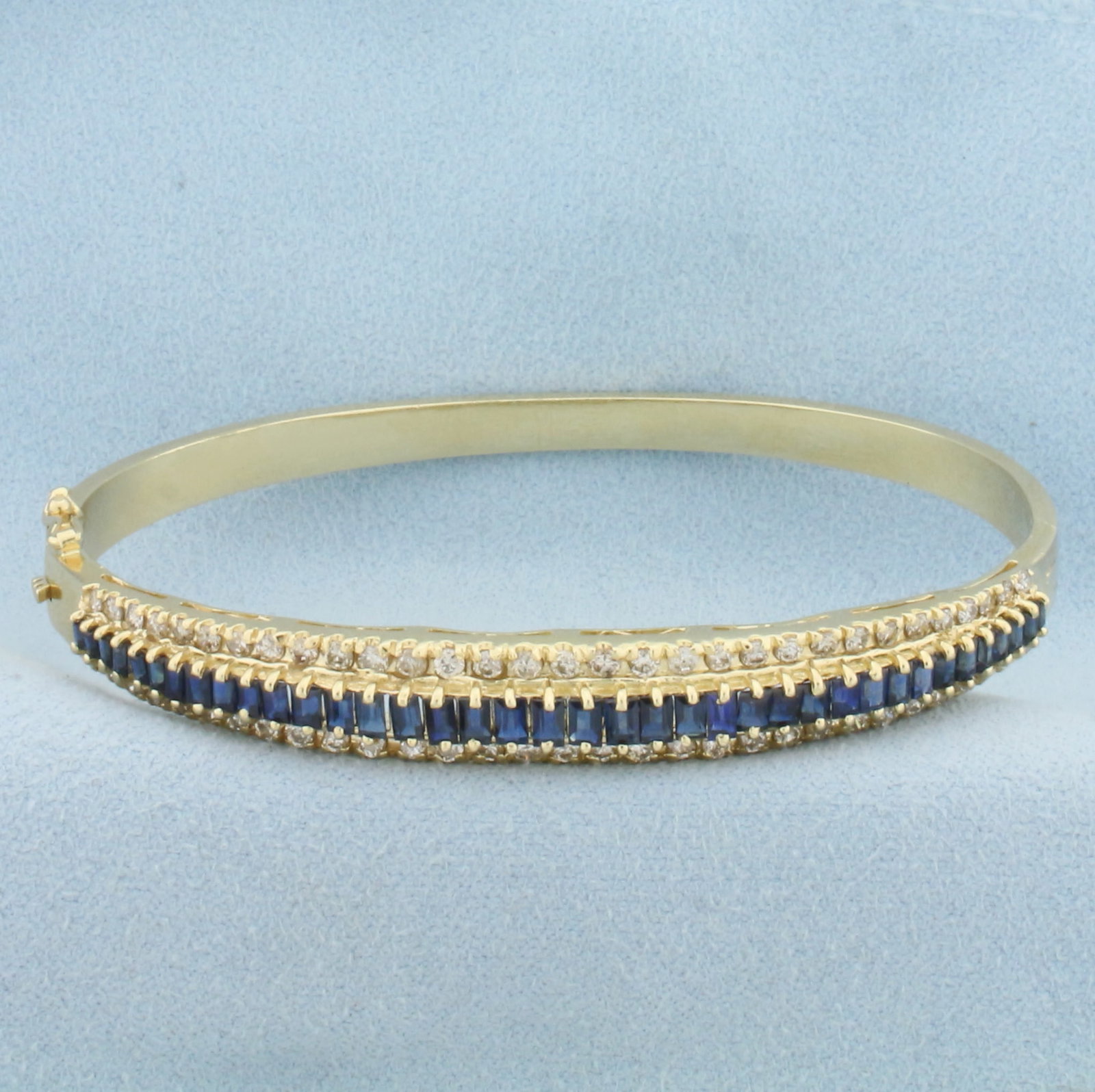 Sapphire and Diamond Hinged Bangle Bracelet in 14k Yellow Gold: In 14k Yellow Gold. Contains thirty-eight high AAA quality emerald cut natural Sapphire gemstones, approximately 3ct TW, with intense color and excellent clarity. Also contains sixty-two .01ct high qu