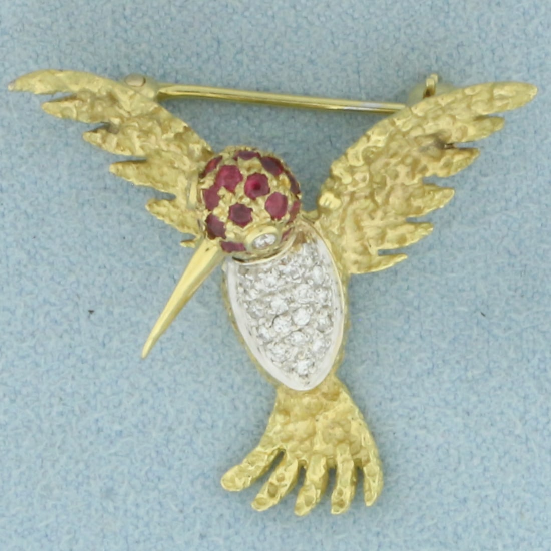 Hummingbird Diamond and Ruby Brooch in 18k Yellow Gold: In 18k Yellow Gold. Contains twenty 1.5mm high quality natural Ruby gemstones with vibrant color. Also contains two .01ct and nineteen 1/2pthigh quality diamonds.. 1 inch long. 1 1/8 inch wide. 5.3g.