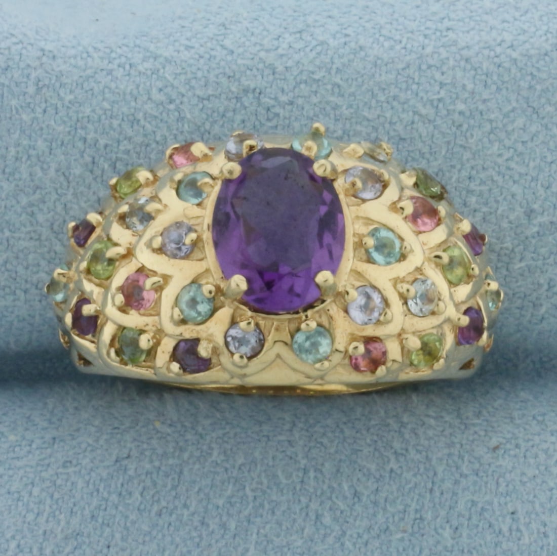 Rainbow Gemstone Bombe Ring in 10K Yellow Gold: In 10k yellow gold. Measures 15mm wide at top of ring. Contains 1 high quality natural 9x7mm Amethyst gemstone with bright color and excellent clarity. Also contains 30 high quality natural assorted 2