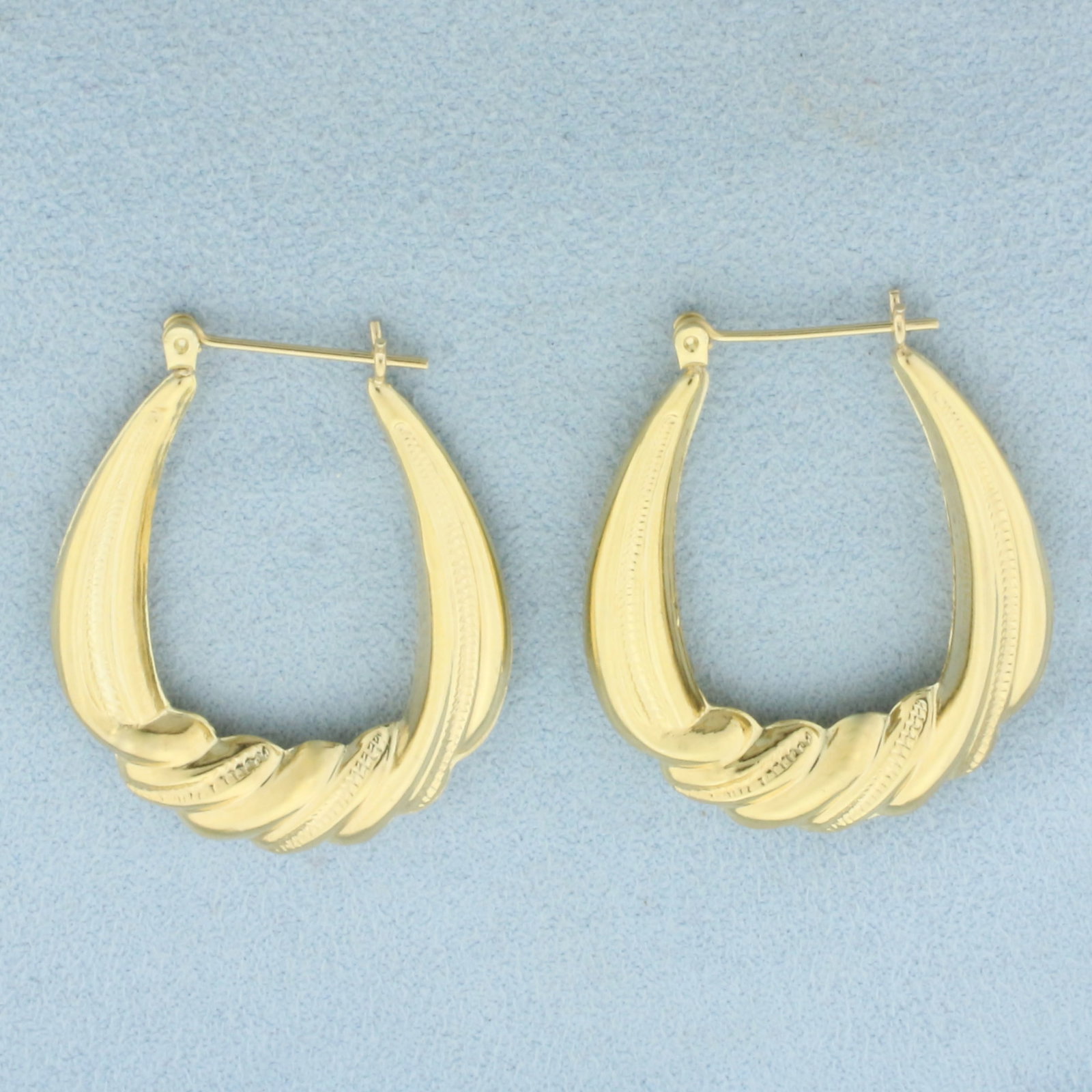 Large Oval Twisting Design Hoop Earrings in 14k Yellow Gold: In 14k Yellow Gold. 1 3/8 inch long. 1 1/8 inch wide. Leverbacks. 3.2g.