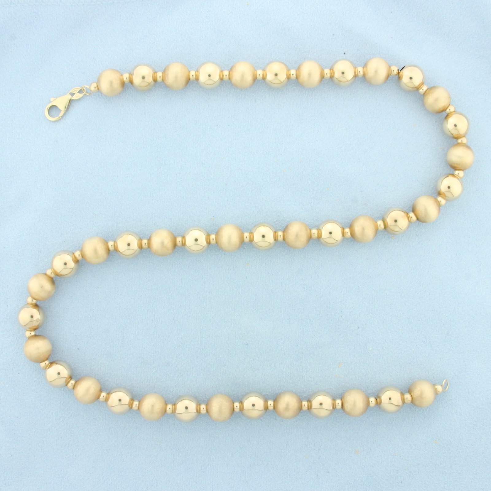 20 Inch Gold Ball Bead Necklace in 14k Yellow Gold: In 14k Yellow Gold. 20 inches long. 10mm beads. Alternating satin and high polish finish gold ball beads for unique look. Lobster clasp. 17.4g.