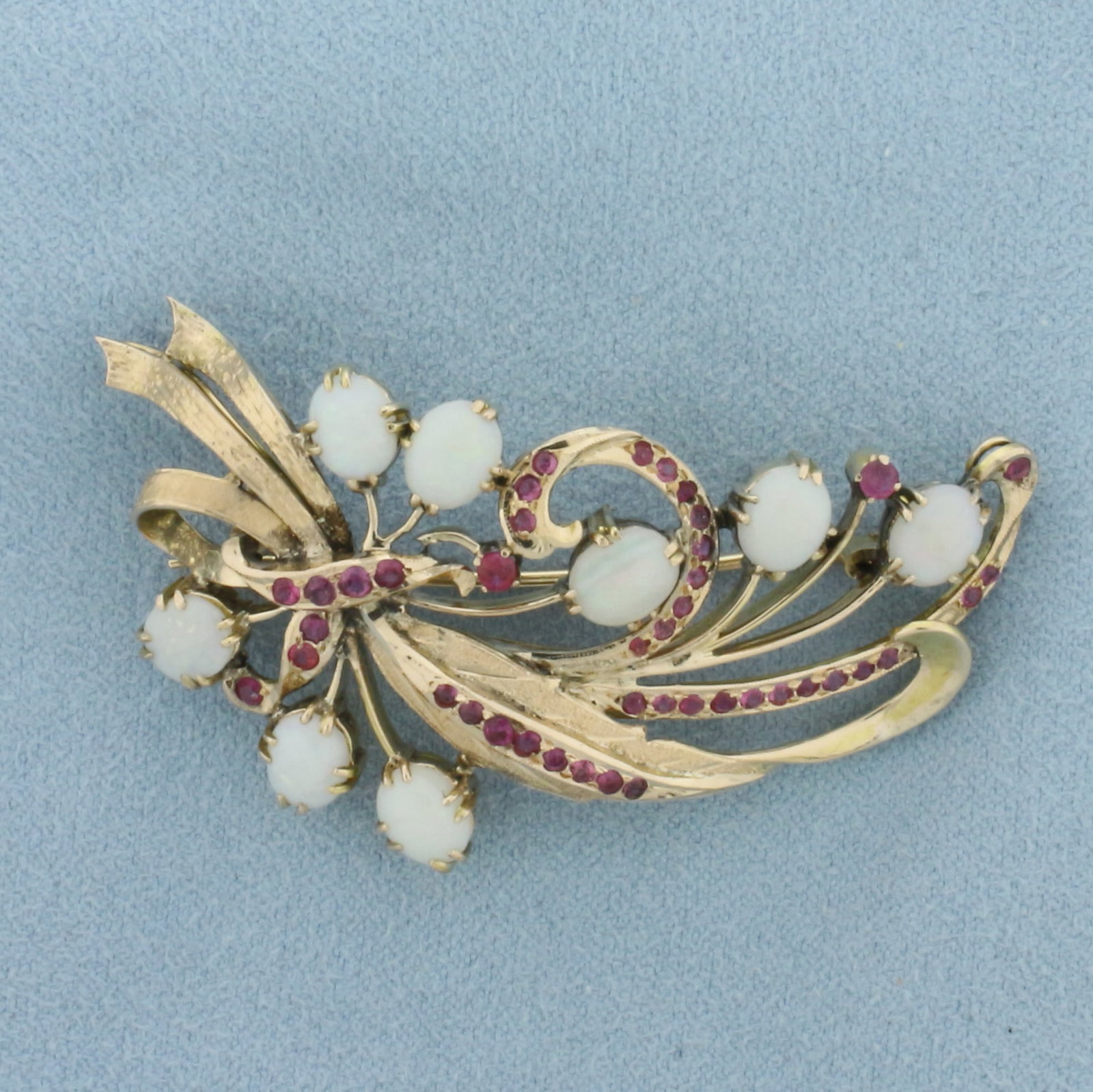 Ruby and Opal Brooch Pin in 14k Yellow Gold: In 14k yellow gold. Measures 2 inches wide by 1 1/8 inches high. Contains 8 oval cabochon opals, 7x5mm each, with excellent play of color, flashes of blue, green, orange, and yellow. Also contains 42 
