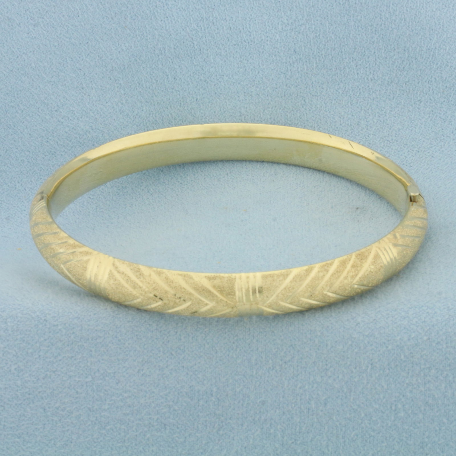Chevron Design Sandblast Finish Bangle Bracelet in 14k Yellow Gold: In 14k Yellow Gold. Interior dimensions: 2 3/8 inch by 2 1/4 inch. 7mm wide. Hinged closure. 10.8g.