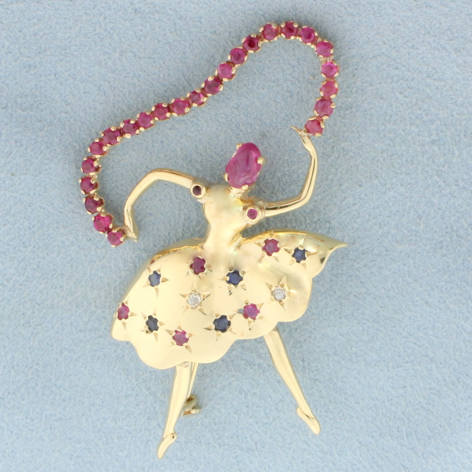 Ballerina Dancer Pin with Ruby, Sapphire, and Diamonds in 14k Yellow Gold: In 14k Yellow Gold. Contains one 6x4mm cabochon Ruby, twenty nine 2mm round Rubies, five 2mm round Sapphires, two .03ct Diamonds, and two 1mm round Rubies. All gemstones high quality natural gemstones