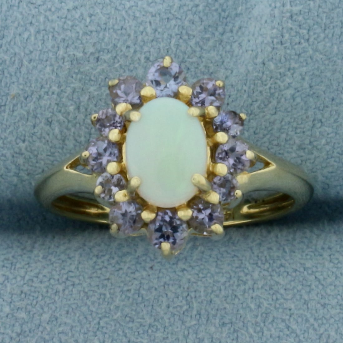 Opal and Tanzanite Halo Ring in 14K Yellow Gold: In 14k yellow gold. Measures 15mm wide at top center of ring. Contains one high quality natural 8x6mm Opal gemstone with excellent play of color, flashes of orange, green, and blue. Also contains 12 h
