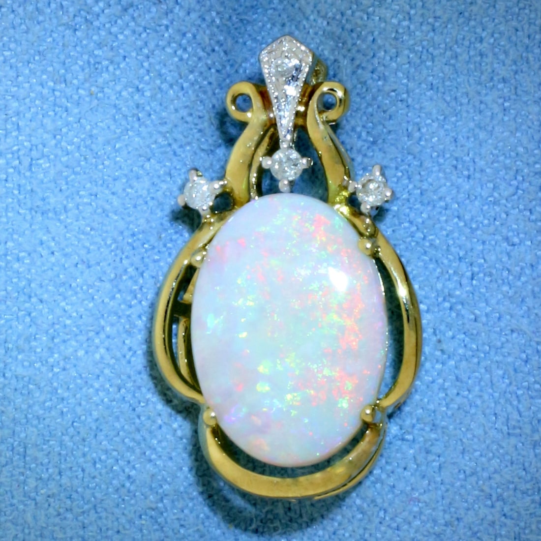 Opal and Diamond Pendant in 14K Yellow Gold: In 14k yellow gold. 7/8 inches long by 1/2 inch wide. Contains 1 high quality natural 15x10mm Opal gemstone with intense play of color, flashes of blue, green, red, and orange. Accented with 4 high qu