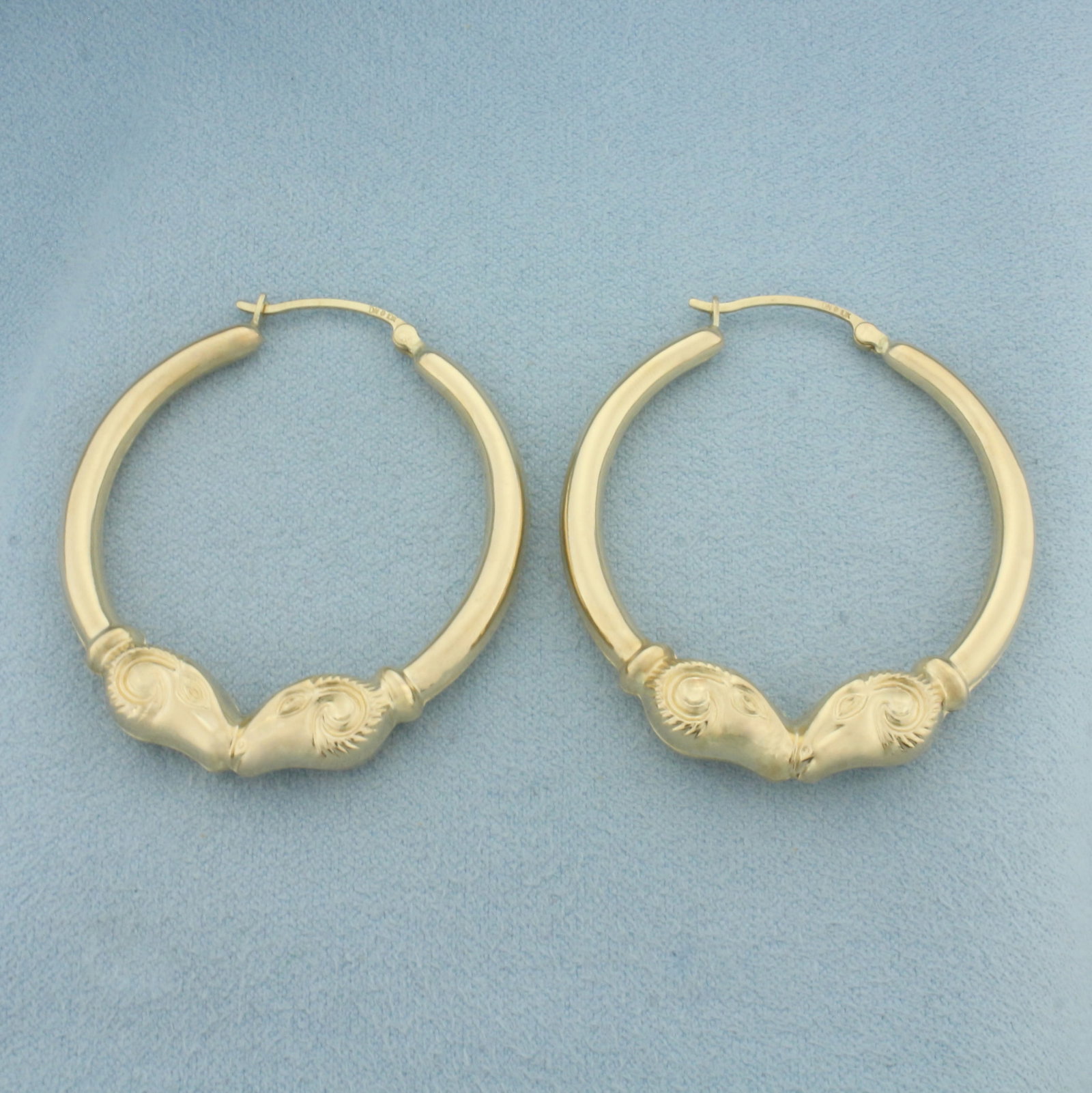 Rams Head Hoop Earrings in 10k Yellow Gold: In 10k Yellow Gold. 1 3/4 inch long. 1 1/2 inch diameter. 8mm thick at widest point. Hinged closure. 4.3g.