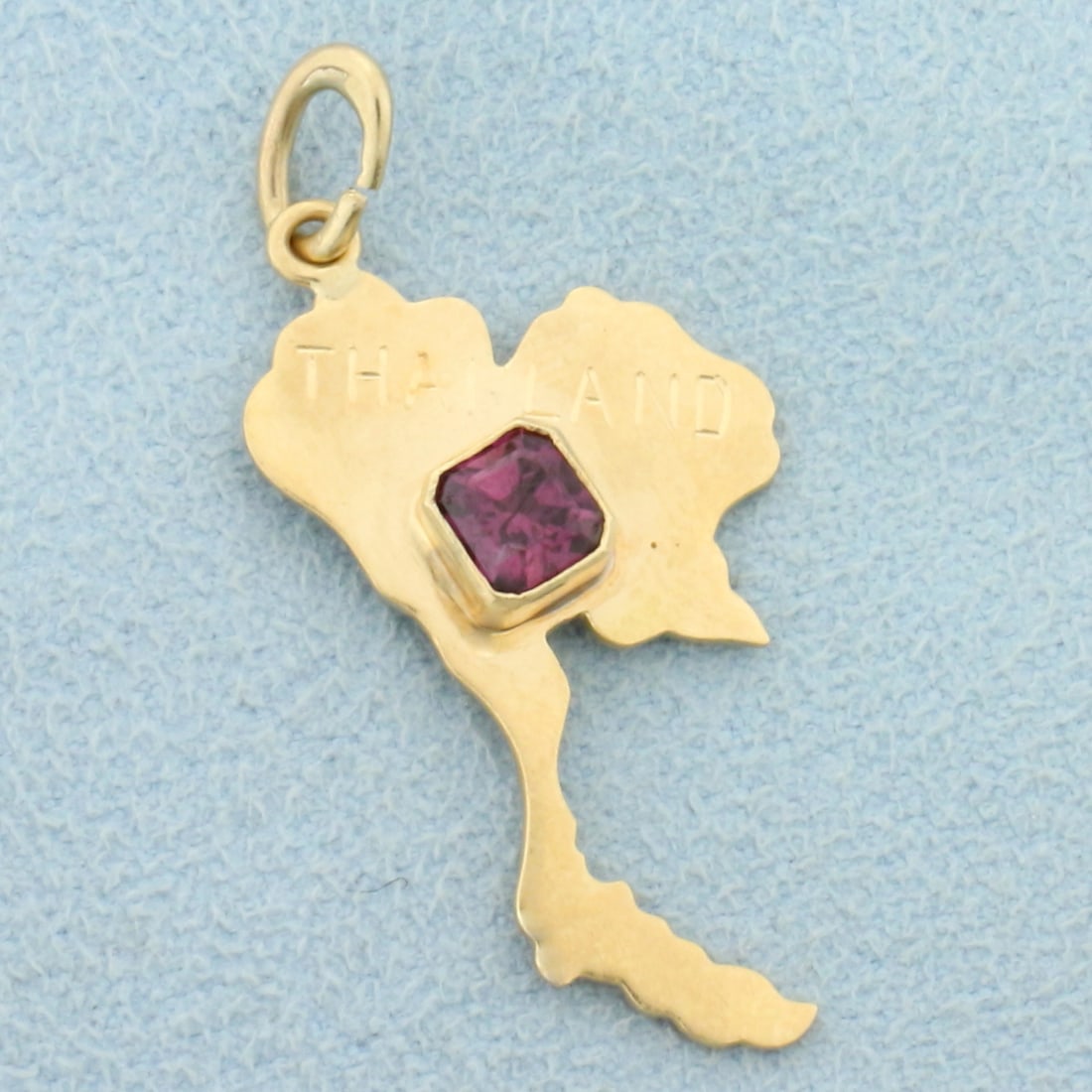 Thailand Ruby Charm or Pendant in 18K Yellow Gold: In 18K Yellow Gold. Contains one high quality natural 1/2ct Ruby gemstone with beautiful ruby red color with hint of purple and excellent clarity. 1 1/4 inches long including jump ring, 3/4 inch wide.