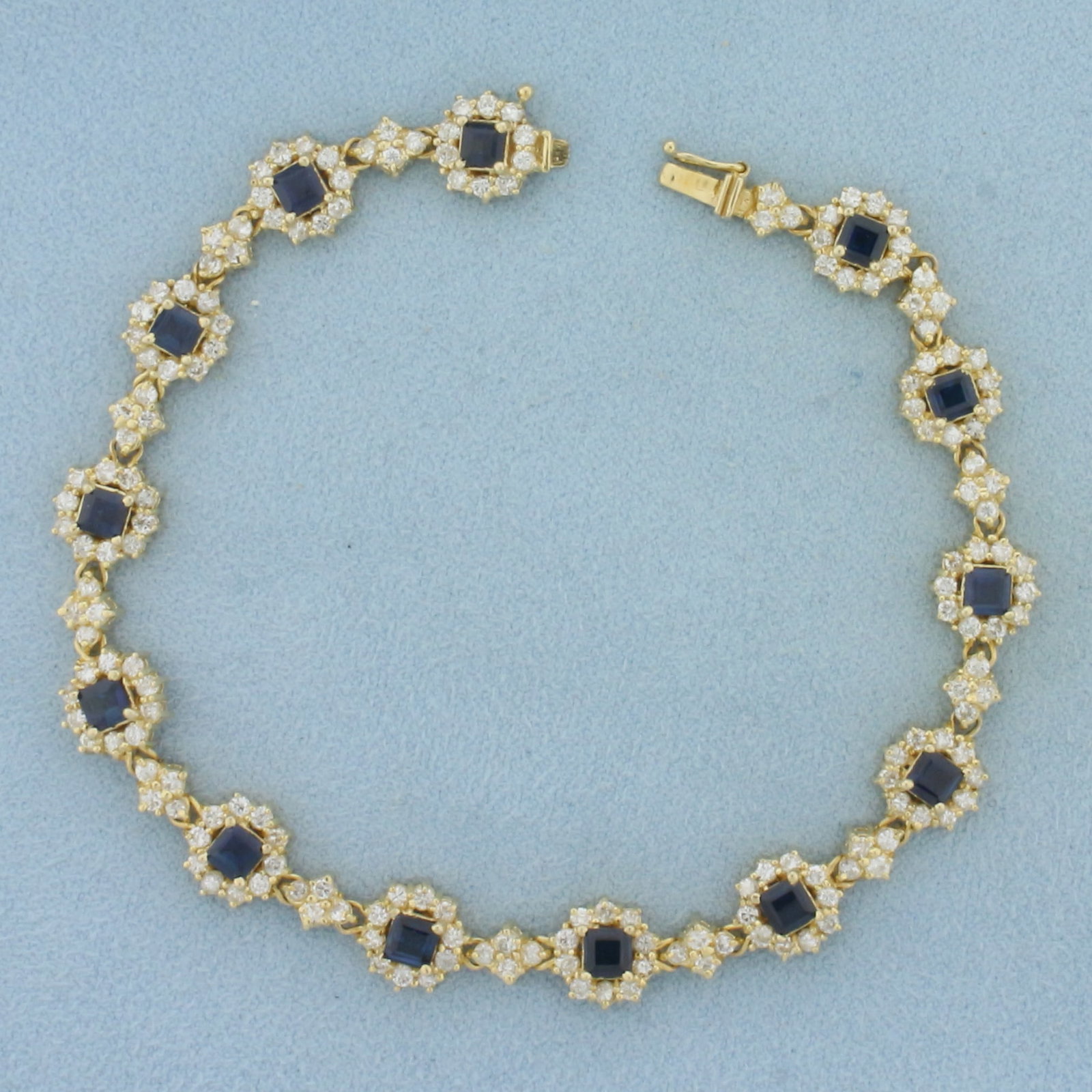 Sapphire and Diamond Halo Tennis Bracelet in 14K Yellow Gold: In 14k yellow gold. 7.75 inches long by 9mm wide. Contains thirteen 3.6mm high quality natural square step cut Sapphire gemstones, with vibrant blue color and excellent clarity. Accented with 181 high