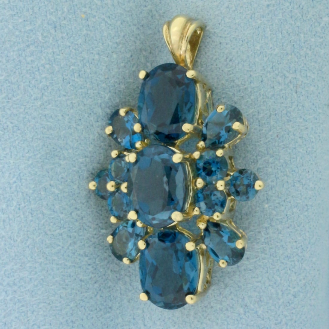 London Blue Topaz Pendant in 10K Yellow Gold: In 10k yellow gold. 1 1/4 inch long by 7/8 inch wide. Contains 3 oval cut 9x7mm, 4 pear cut 6x4mm, and 6 round cut 4mm natural high quality London Blue Topaz gemstones with deep blue color and excelle