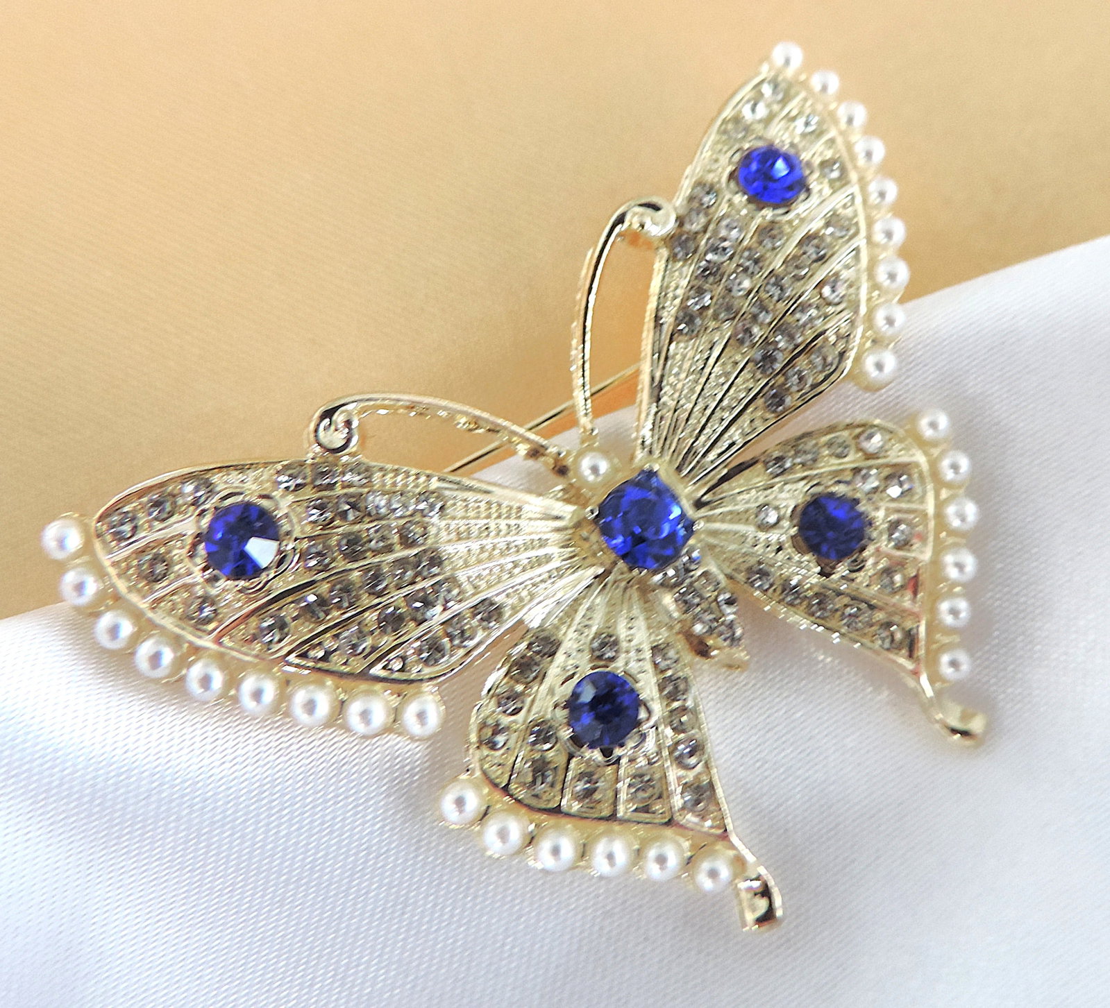 Crystal & Pearl Butterfly Brooch: Title: Crystal & Pearl Butterfly Brooch Description: A pretty gold tone butterfly brooch set with blue & white crystals and faux seed pearls. Measurements: 6cmx3.5cm. Condition: New