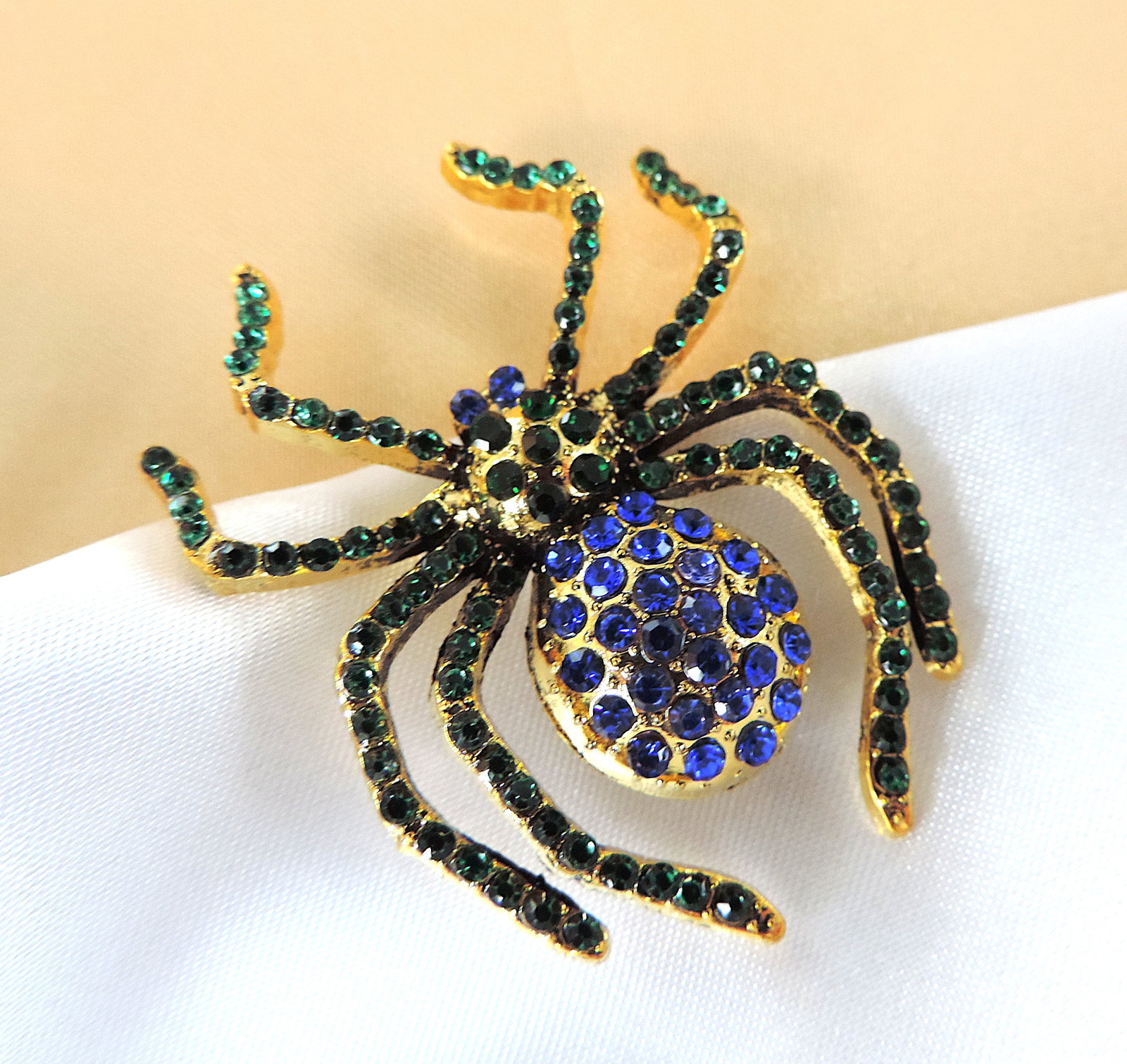 Crystal Encrusted Spider Brooch: Title: Crystal Encrusted Spider Brooch Description: A gold tone spider brooch set with blue & green crystals. Measurement: 4.5 x 4.0cm Condition: New