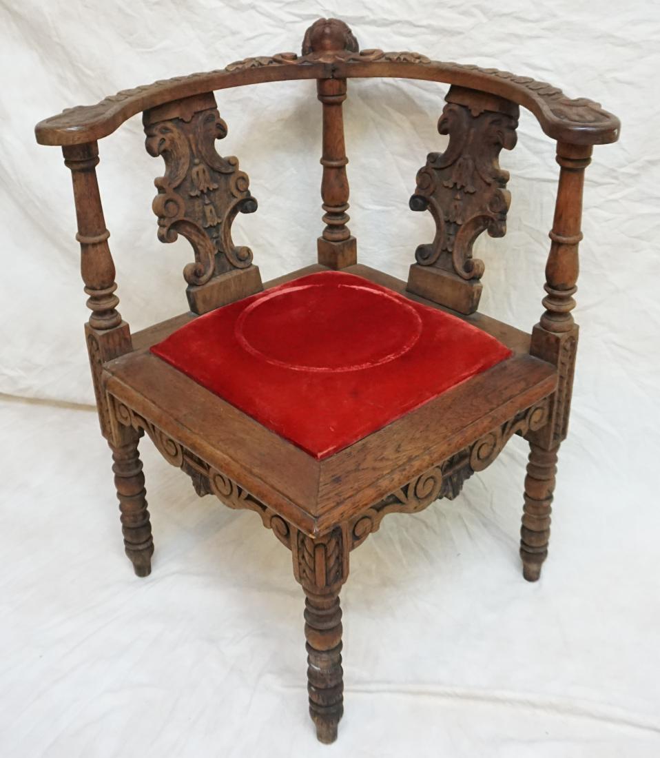 ANTIQUE ENGLISH FIGURAL CARVED OAK CORNER CHAIR: English carved oak corner chair, 19th c., the curved crest rail centering a figural mask, dual splats carved with griffins, padded seat with worn red velvet upholstery, all rising on turned supports.