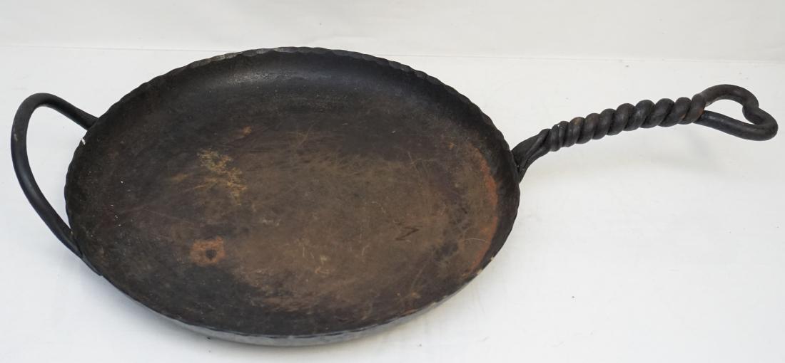 LARGE HAND FORGED CAST IRON SKILLET: Antique American Primitive Large Hand Forged Cast Iron Skillet. Pie crust rim, twisted heart handle. Measures 23:long, 14"wide. Weight 8 pds PROVENANCE: A Private Charleston SC Estate.