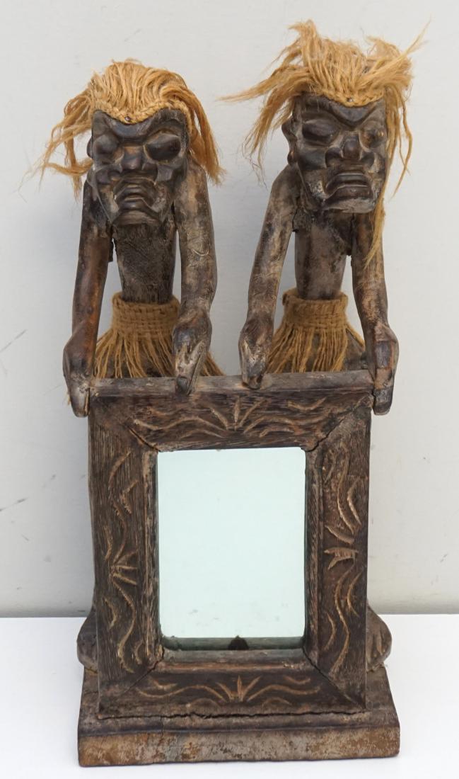 PAPUA NEW GUINEA CARVED FIGURES: Mid Century Hand Carved Wood Two Figures with Raffia Hair and Skirts holding a frame with mirror. Measures 6 1/2"x5"x13 1/2" Weight 2 pds. 5 oz. PROVENANCE: A Charleston SC Private Estate.