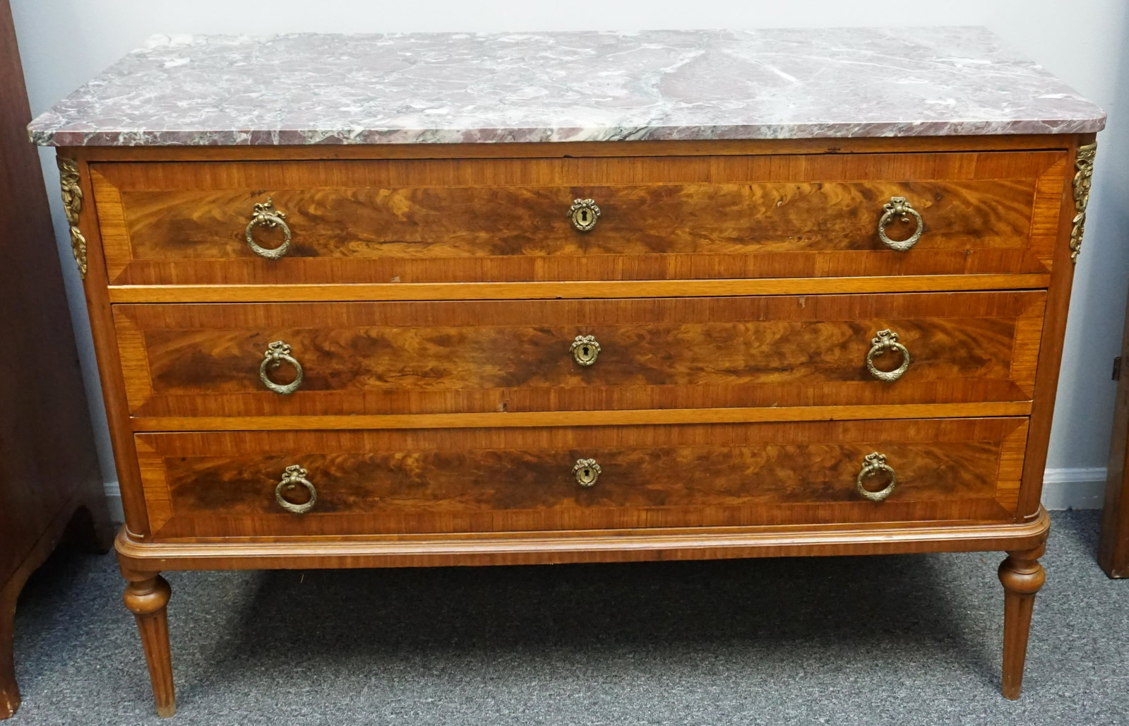 BRONZE MOUNTED MARBLE TOP FRENCH CHEST / COMMODE: Antique French Red Marble Top Satinwood Chest / Commode with rounded front corners, over corresponding case fitted with three drawers, bronze ormolu mounted corner posts continuing into tapered legs. 