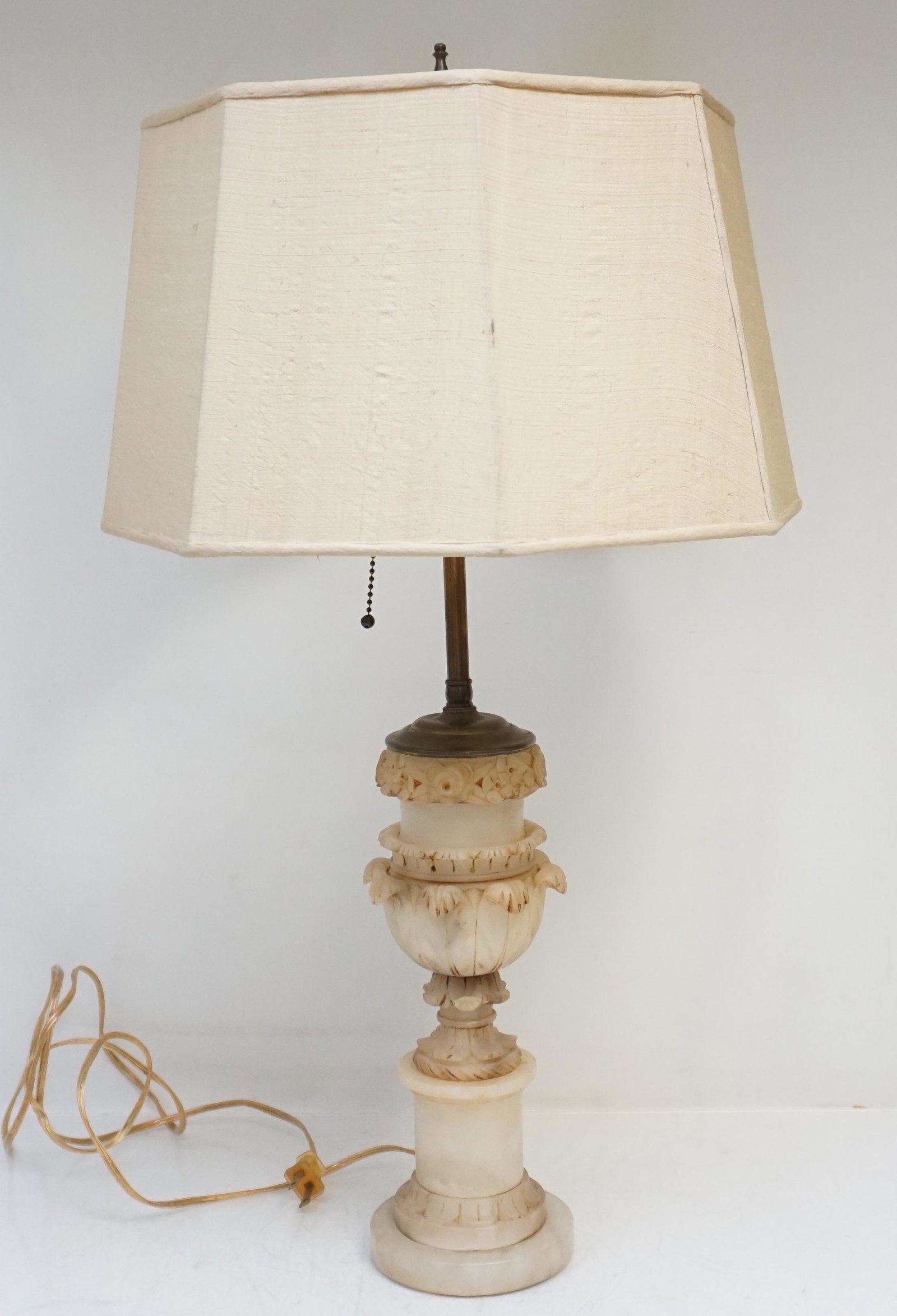ANTIQUE ITALIAN ALABASTER RELIEF LAMP: Antique Hand Carved Relief Italian Alabaster Lamp. Having a design of carved flowers and acanthus leaves. Measures 5"x5"x22". Silk Dupioni shade, somewear, 15"x15"x9". Weight 7 pds. PROVENANCE: A Char