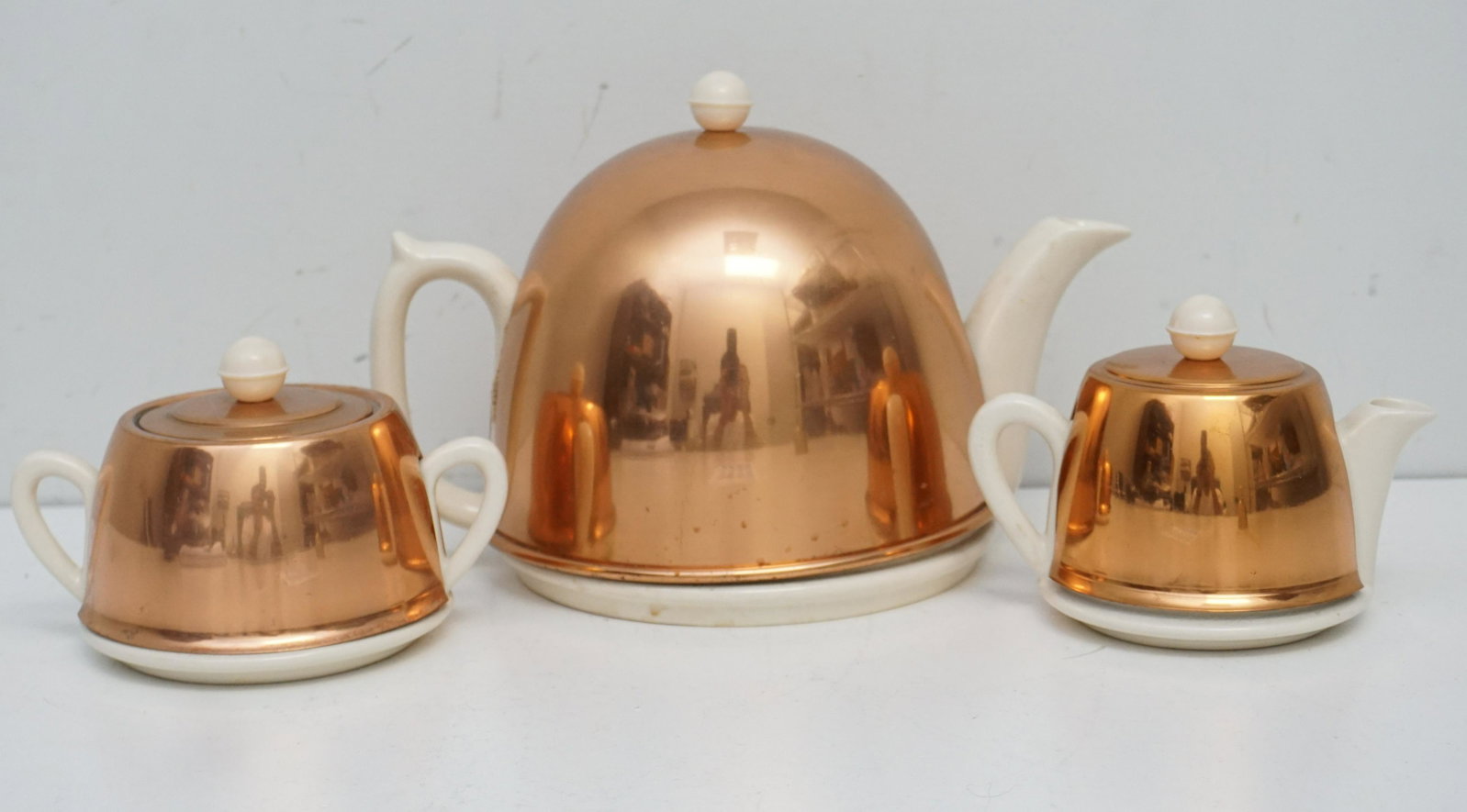 3 PC ENGLISH COPPER COSY & PORCELAIN TEA SET: Three Piece English Art Deco Tea Service. Art Deco Teapot with copper cozy & wool insulator. Cream and Sugar, all with bakelite finials. Very good condition. All marked Made in England. Weight on all 