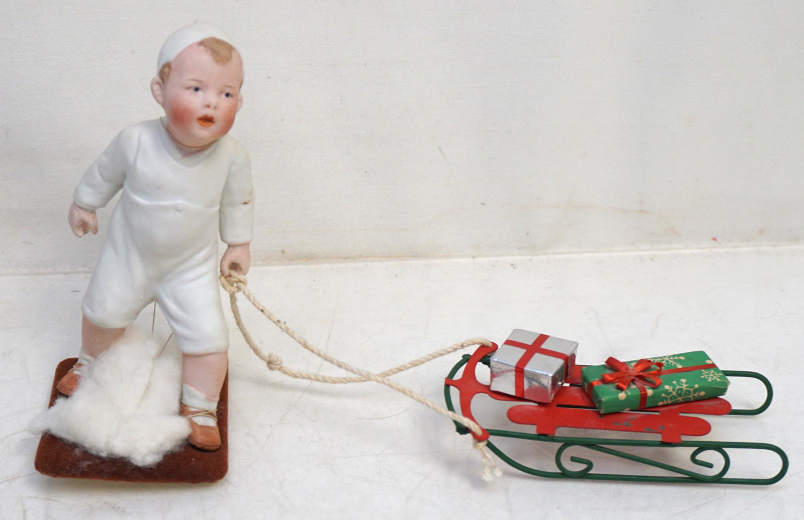 VINTAGE HEUBACH PORCELAIN CHRISTMAS CANDY: Vintage Original Heubach Porcelain Bisque Boy with Christmas Sled. We believe he may of been the top of a Candy Container Boy 6" tall Sled 4 1/2" long. Weight 6 oz. PROVENANCE: A Private Charleston SC