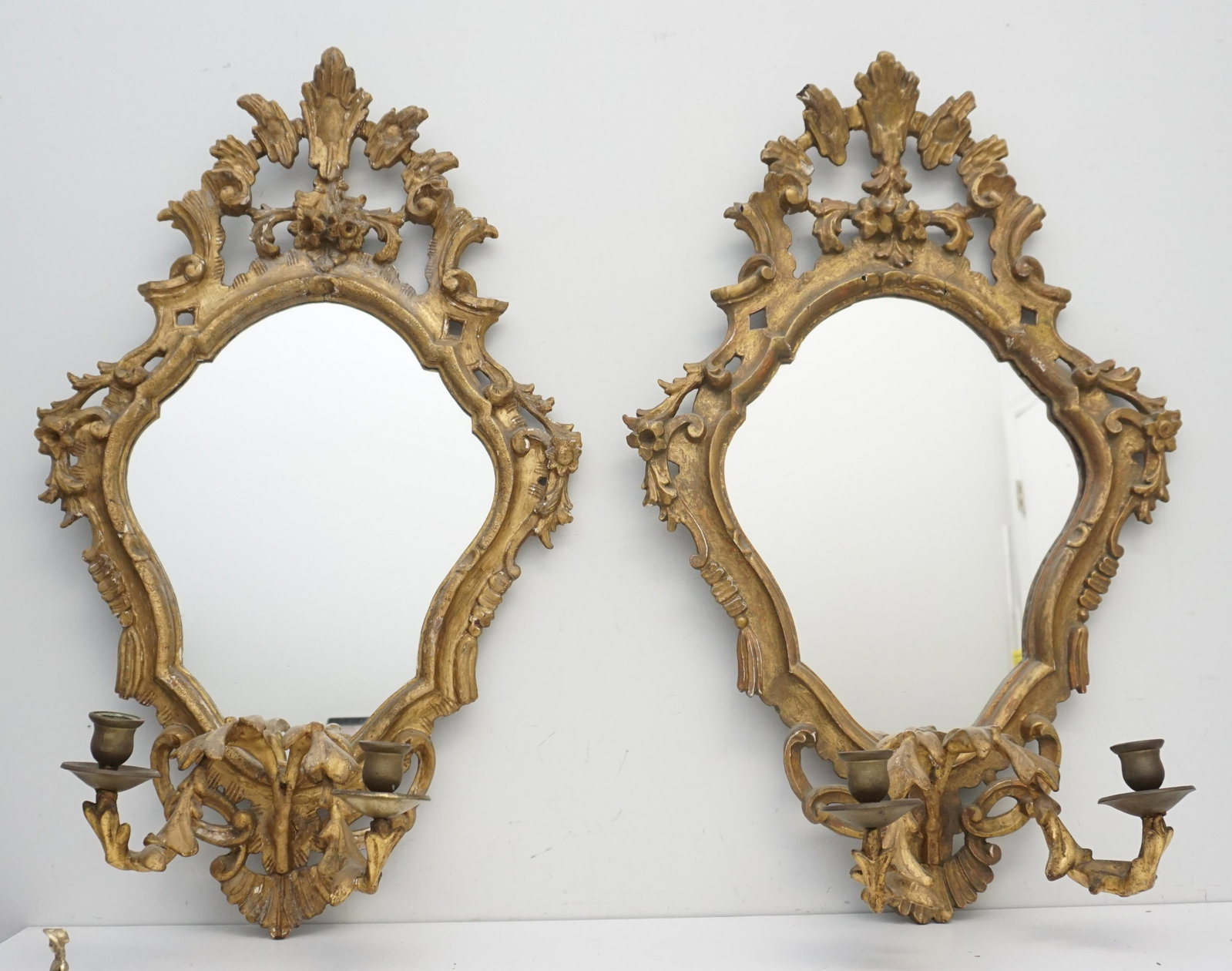 PAIR CARVED GILTWOOD MIRRORED 2 LIGHT WALL SCONCES: A Pair of 19th c. Rococo Style Giltwood Mirrored Sconces, Height 32". 19th century, of cartouche form, having carved C-scroll and foliate decoration, each with 2 candle holders. Some wear and scattere