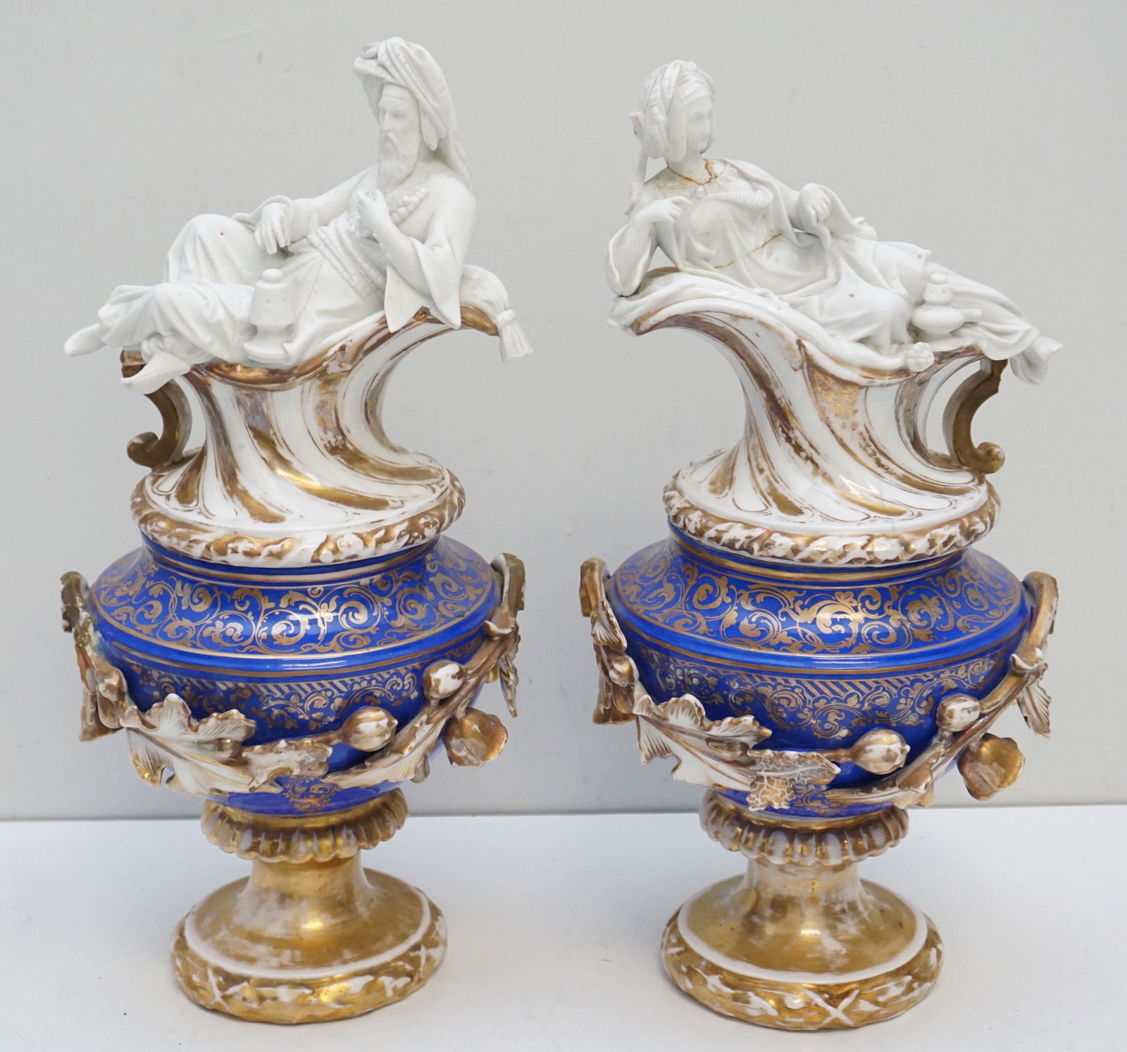 PAIR ANTIQUE JACOB PETIT OLD PARIS URNS: Pair of Antique Jacob Petit Figural Lidded Urns. Sultan and Sultana Reclining Figural Lids, Man and Woman. Some repairs and loss. Each approximately 15 1/2". Weight 10 pds 8 oz. PROVENANCE: The Estate