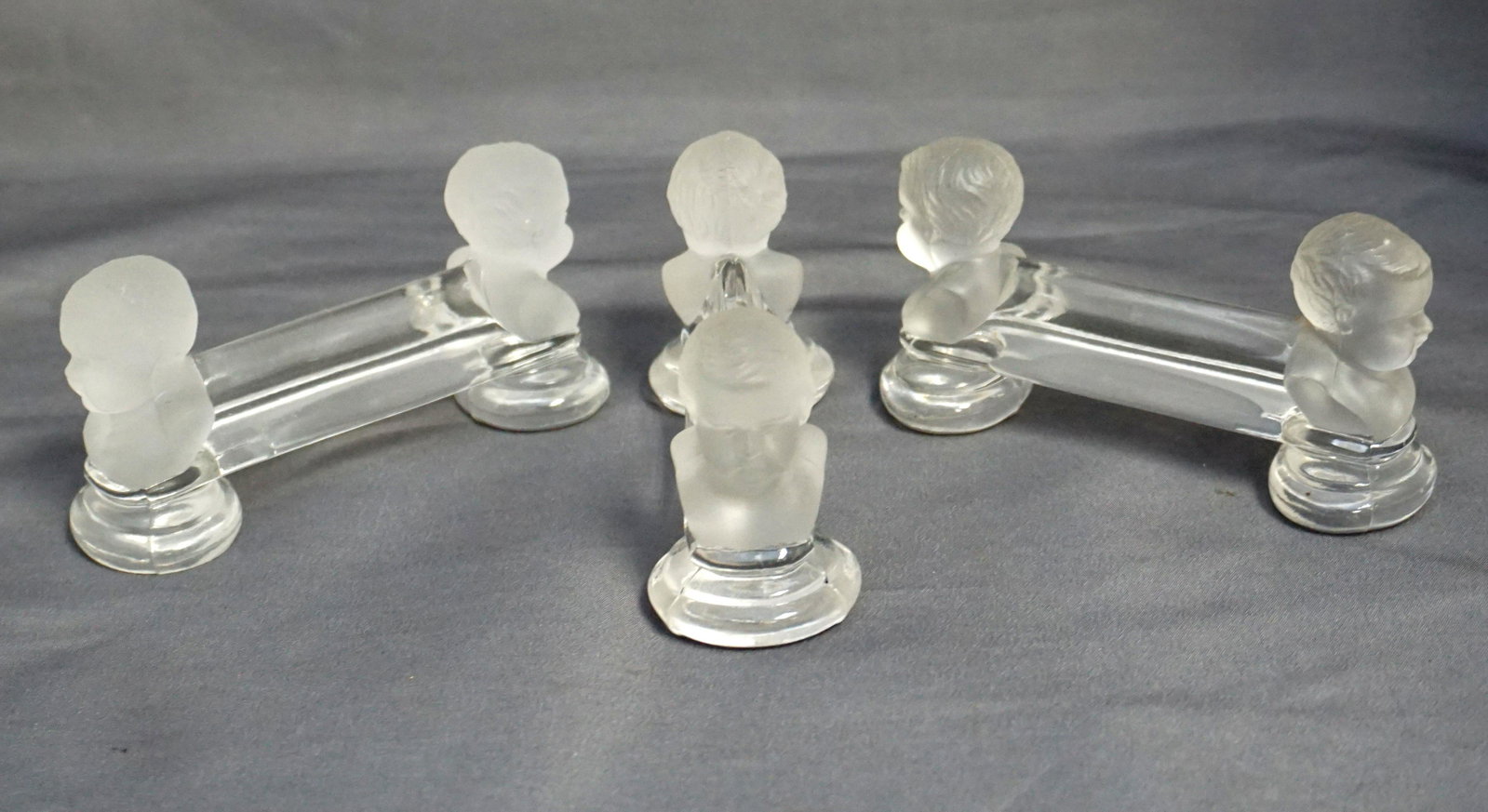 3 BACCARAT CHERUB PORTE COUTEAU: A set of three Cherub Porte Couteau, or knife rests, Baccarat Crystal, France, 1907. The rests show a center bar in clear crystal supported by satin finished busts of cherubs at either end. The busts 