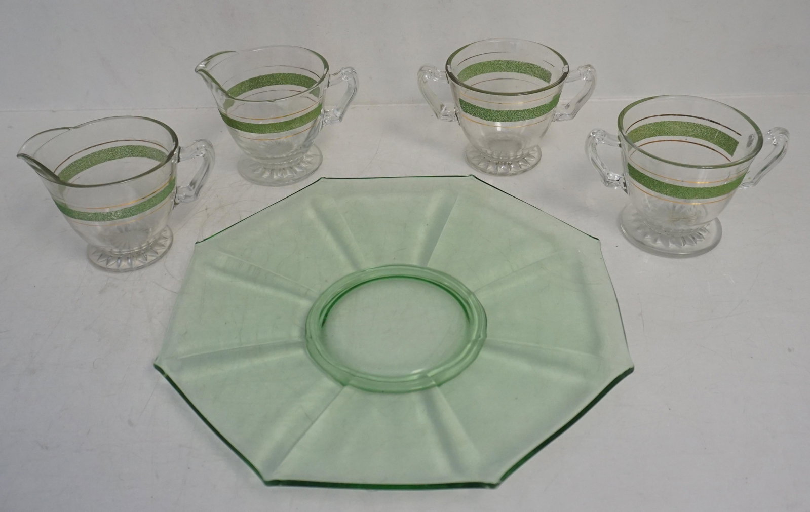 GLASS LOT VASELINE CAKE PLATE + 2 SETS CREAM & SUGAR: Vaseline Footed Cake Plate 11"x11". Two sets of Clear Depression Glass Cream and Sugar with Green Textures Stripe 3 1/4". Weight on all 3 pds 4 oz. PROVENANCE: A Charleston SC Private Estate