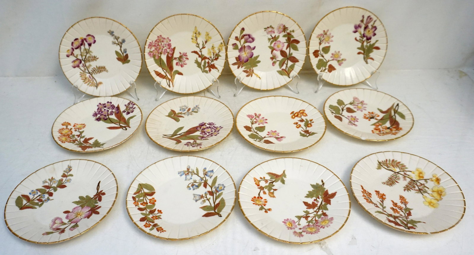 12 c 1880 ROYAL WORCESTER DESSERT PLATES: Twelve blush ivory Royal Worcester dessert plates circa 1880. Hand painted various florals, each feature two distinct plants, painted as in a botanical drawing, fluted sides and gilded rims. 1 with ch