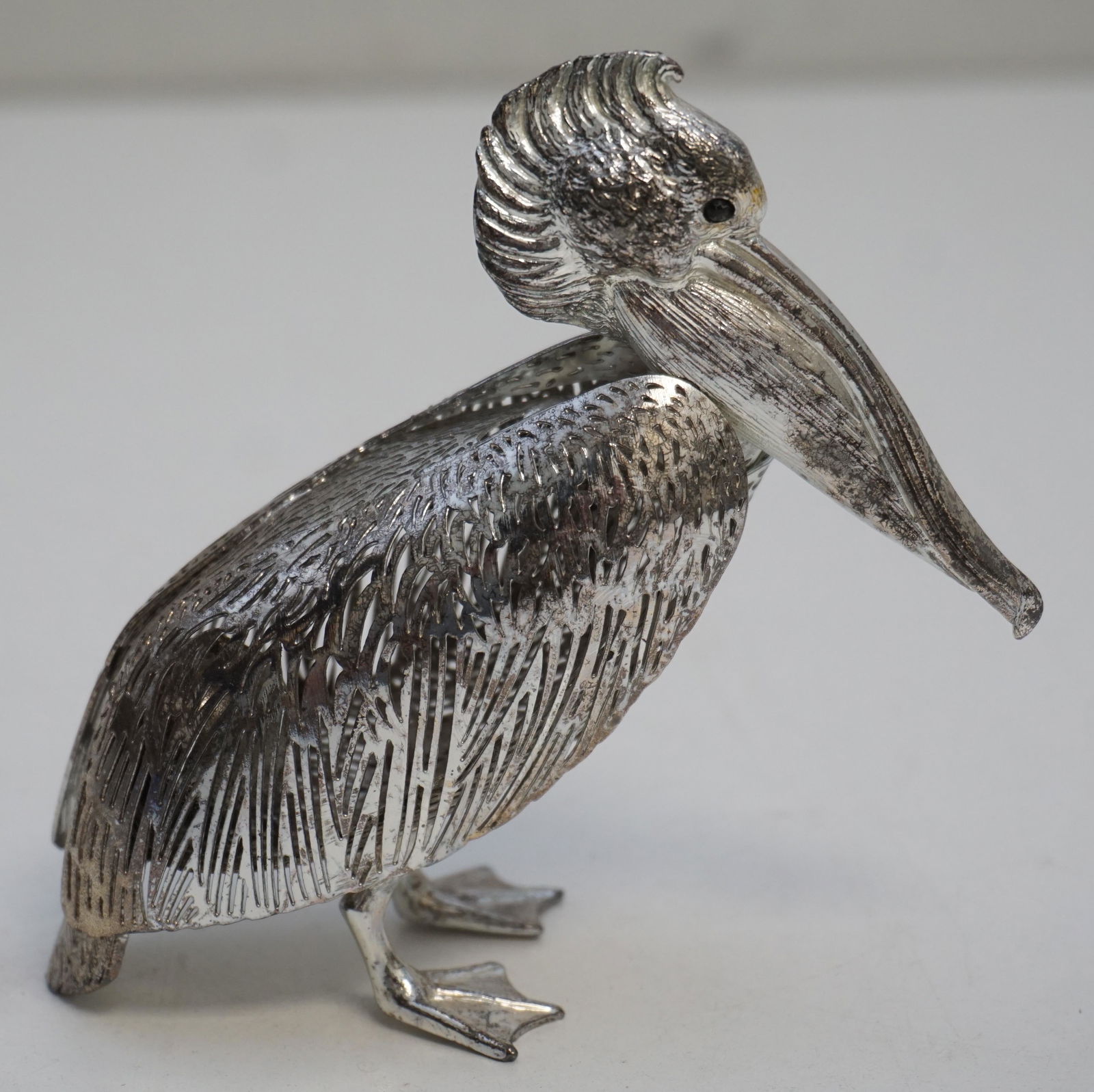 CHRISTOFLE SILVER PLATED PELICAN: A silver plated christofle figurine depicts a pelican with pierced work and finished with onyx eyes, retailed by Neiman Marcus. Stamped underneath the tail "Christofle France", H: 4 3/8" L: 4 1/2". We