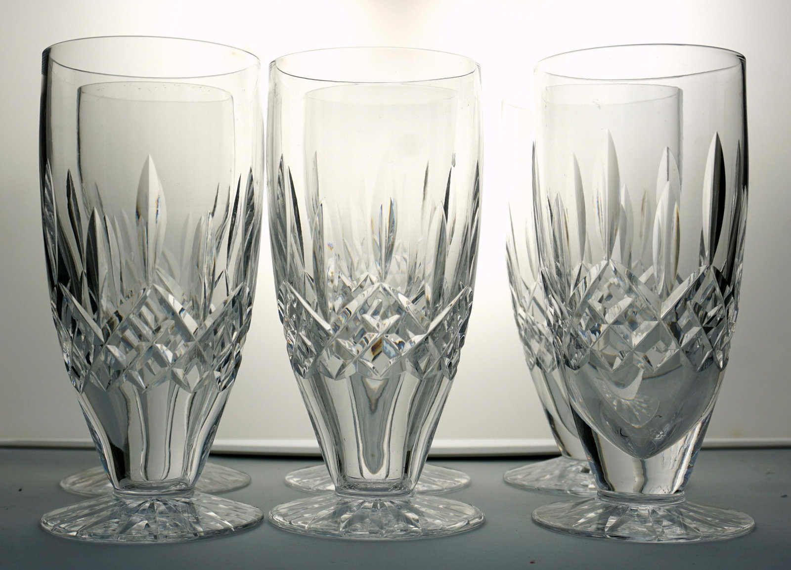 6 WATERFORD LISMORE ICED TEA GLASSES: Set of six (6) Waterford crystal iced tea glasses in the Lismore pattern. All with a series of staggered wedge-cuts with a band of cross hatch cuts below to the bowl on a cut foot. Acid etched maker's