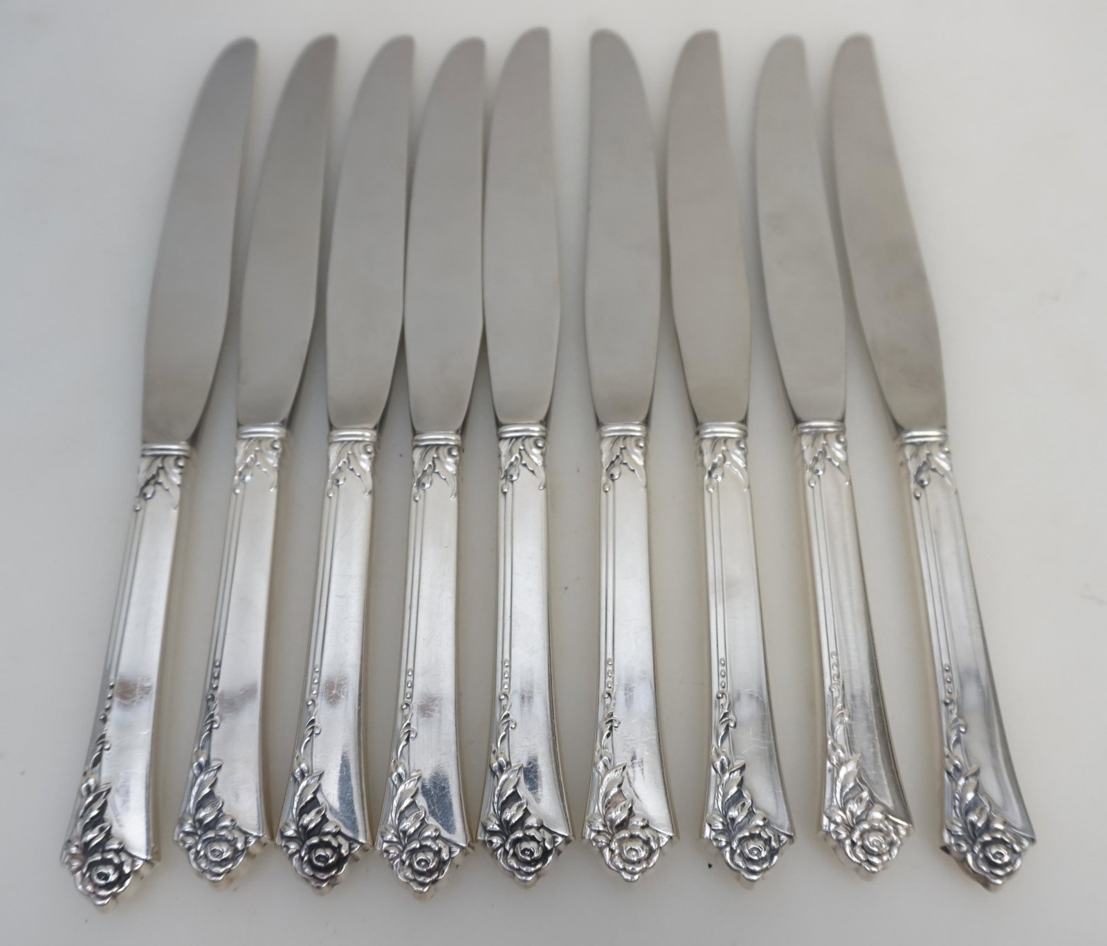 9 STERLING DAMASK ROSE KNIVES: 9 Sterling Silver Handle Stainless Blades Dinner Knives in the 1946 Damask Rose Pattern by Oneida Silversmiths. Good condition. No monograms. Each 8 7/8". Weight on all 1 pd 4 oz. PROVENANCE: Edwin Mo