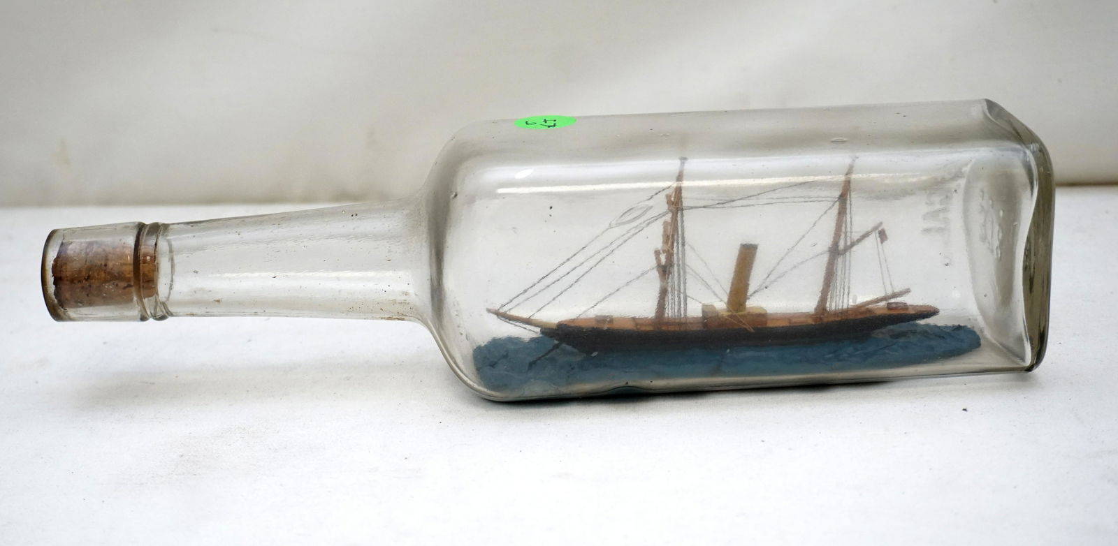 ANTIQUE AMERICAN SHIP IN A BOTTLE: Antique American Ship in a Bottle. 2 Masted Steamship. Bottle label from 6th Ave New York Liquor Store. Late 19th, early 20th c. Bottle 11 1/4" long. Weight 1 pd 4 oz. PROVENANCE: A Charleston SC Priv
