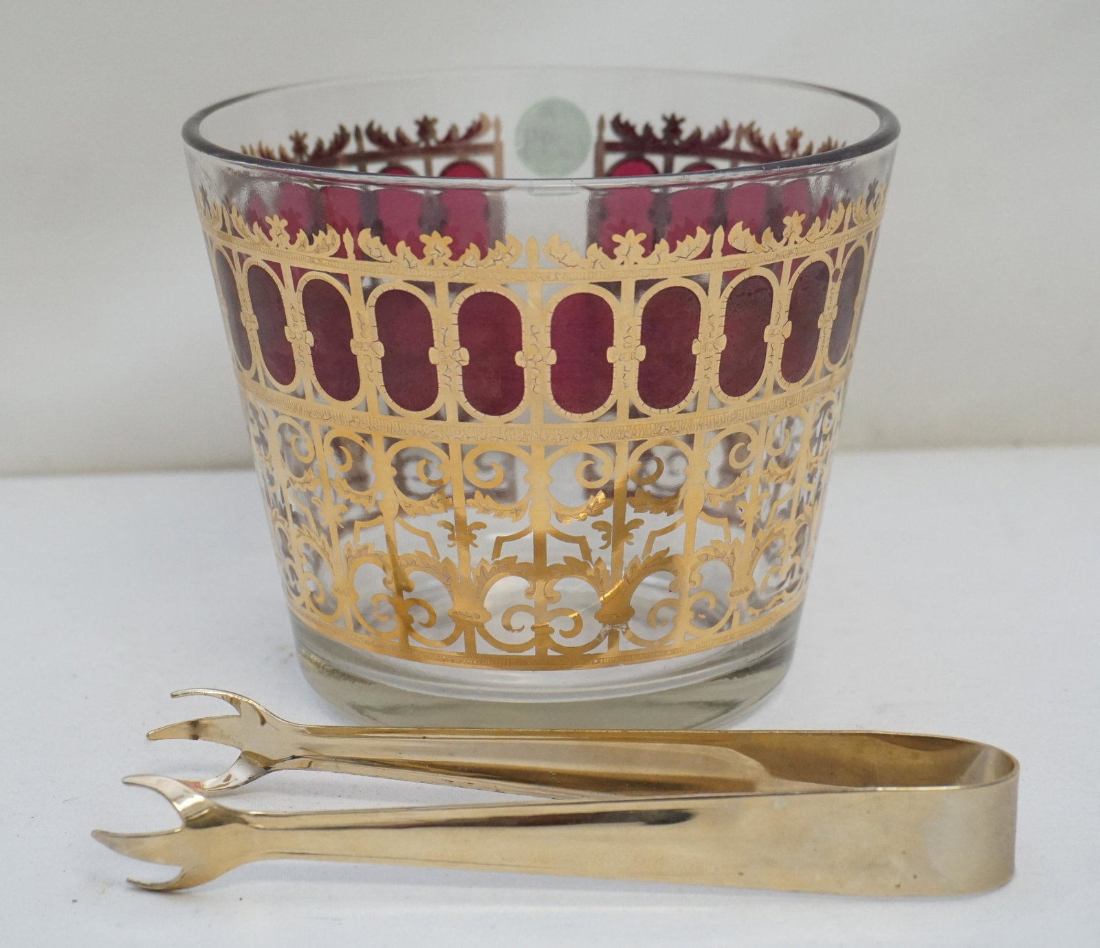 VINTAGE CULVER MID CENTURY 22k ICE BUCKET: Mid Century Culver Cranberry and 22k Scroll Ice Bucket and Tongs Gold Overlay. Bucket 6"x4 3/4". Tongs 6 1/2". Weight PROVENANCE: A Charleston, South Carolina Private Collection. Culver Ltd was a glas