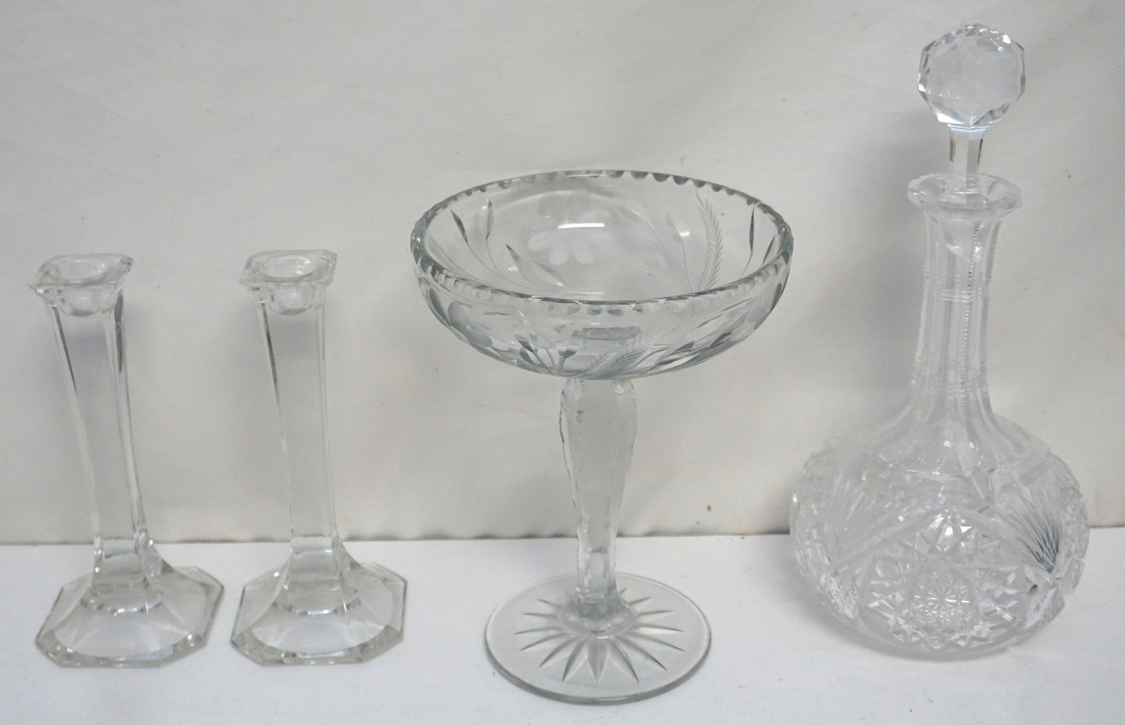 4 pc GLASS DECANTER -COMPOTE - CANDLESTICKS: All are Vintage. 1- Cut Glass Decanter Hobstar with Fan, Zipper Neck. Stopper is chipped on bottom. 11". 2- Cut and Etched Glass Tall Compote 6" wide 8" tall. 3- Pair Glass Candlesticks. 7". Weight on