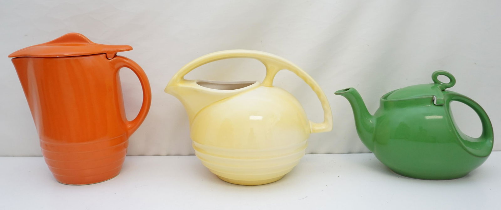 3 pc VINTAGE FIESTAWARE PITCHERS: 3 Vintage 1950s Fiestaware / Hall Pitchers / Teapot. 1- Hall Green Teapot 8 1/2" long. 2- Yellow Pitcher, very small hairline to lip 9" long. unmarked. 3- Orange Pitcher Unmarked 9" tall. Weight on al