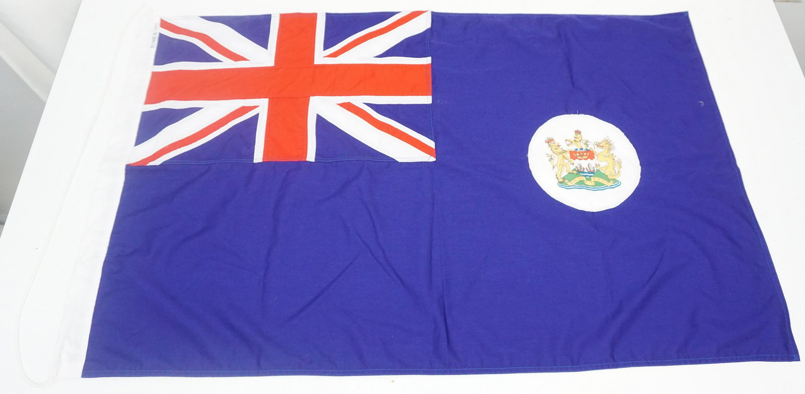 VINTAGE COLONIAL HONG KONG FLAG: Vintage Official Colonial Hong Kong Flag with images depicting the Union Jack and the Seal of Hong Kong. Last flown on July 1, 1997 when Hong Kong was handed over to China, Measures 37"x24". Weight 4 