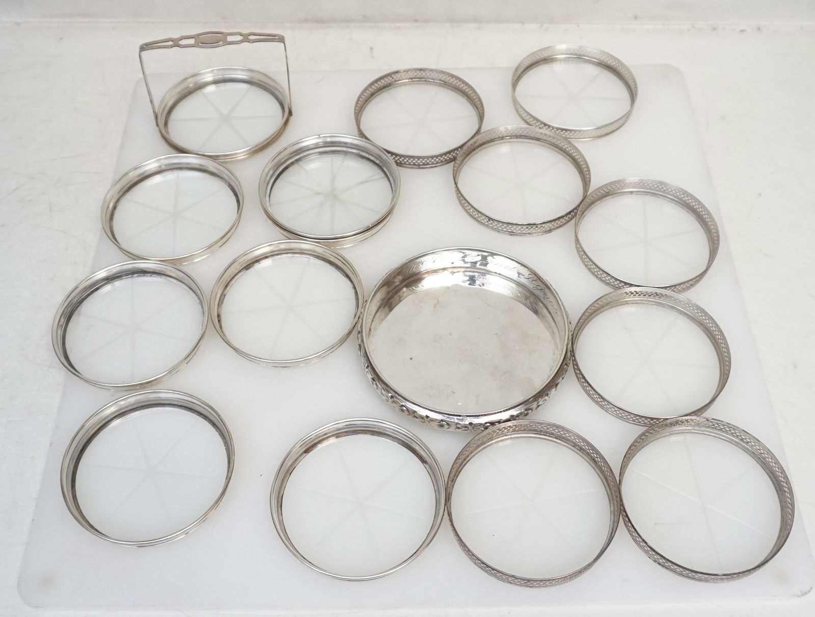 16 pc STERLING COASTERS: 1- Sterling Silver Chased Wine Coaster, engraved to inside rim McColl and Agnes 1944. Measures 4", weight approximately 75 grams. 2- Set of 8 Matching Sterling Silver Rimmed and Glass Coasters in Cadd