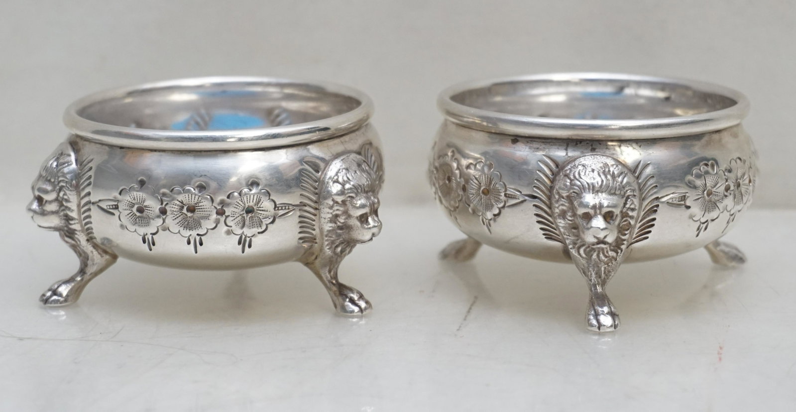 PAIR HAND CHASED STERLING SILVER LION SALT CELLARS: Matched Pair of Very Fine Ornate Antique American Hand Chased Sterling Silver Salt Cellars. Figural Lion Heads and Feet, Florals. No monograms. Each 2 1/2"x2 1/2"x1 1/2". Weight combined approximately
