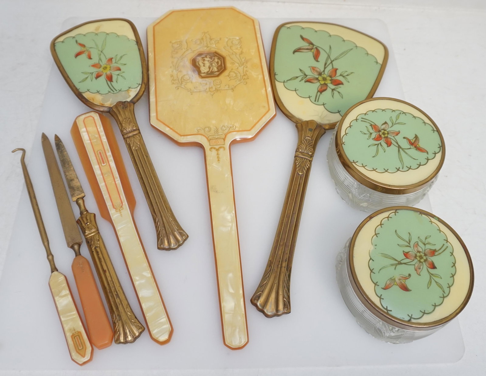9 PC ART DECO VANITY ITEMS: Both are Art Deco Era. 1 Five Piece Set and 1 4 Piece Vanity Set. 5 piece Set with 2 glass powder/cream jars 3 1/2"x2". Beveled Hand Mirror 12 1/2". Brush 9 3/4" and Nail File 8 1/4". 4 Piece Dupont L